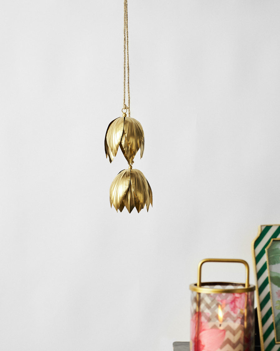Two gold lotus bells hanging from jute in a room beside a lantern