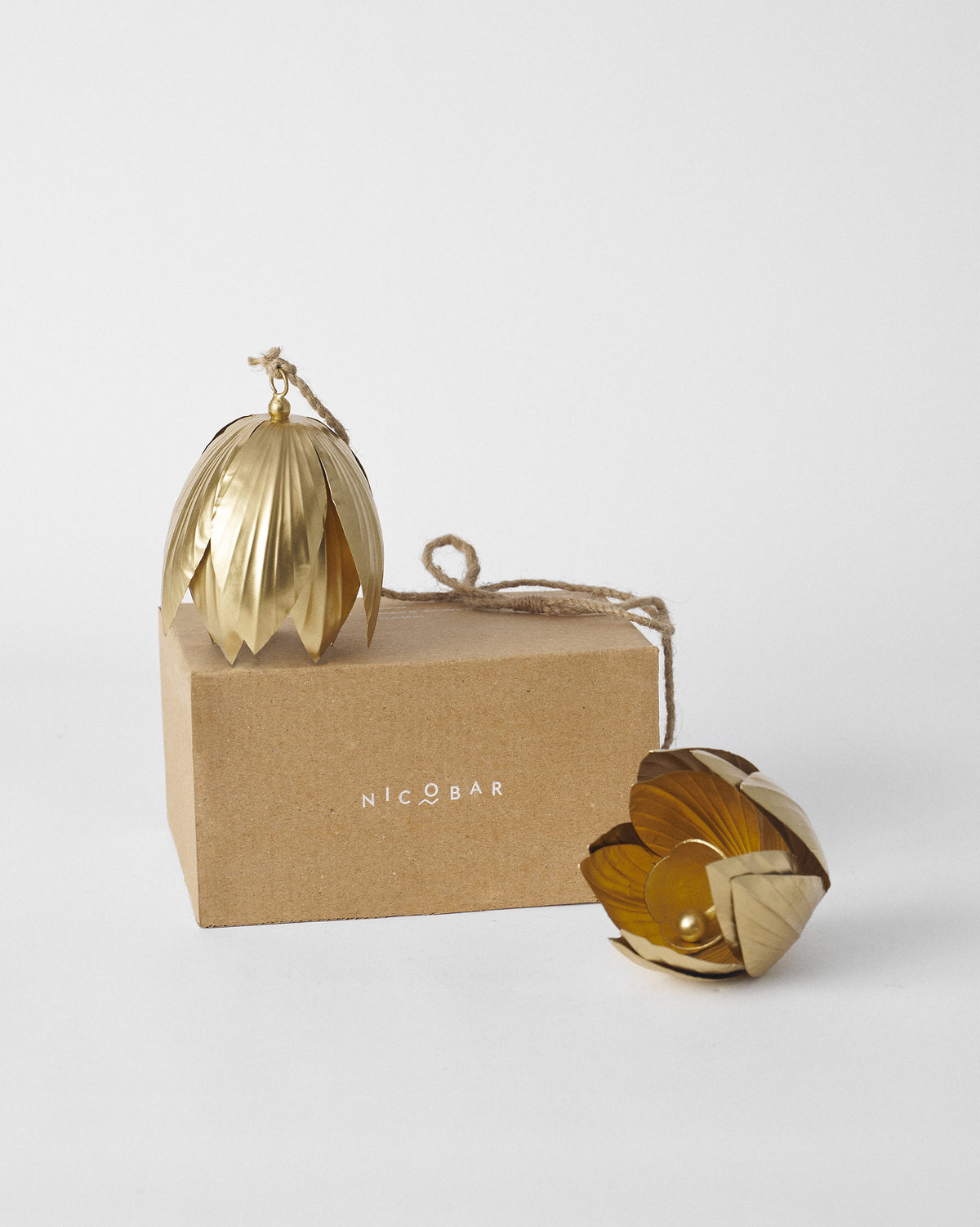 Gold lotus bells with jute cords shown with a brown Nicobar gift box.