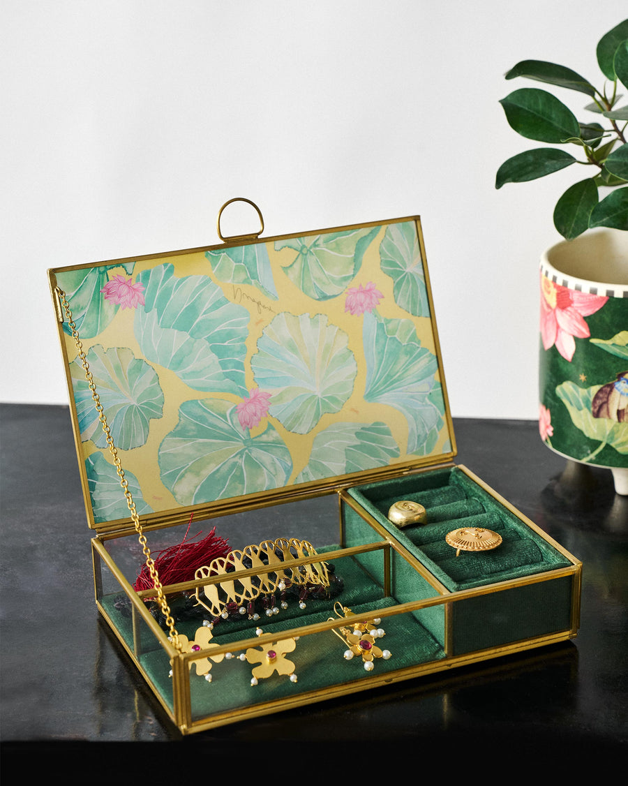 The open Lily Pond box holding gold jewellery on a dark table beside a plant