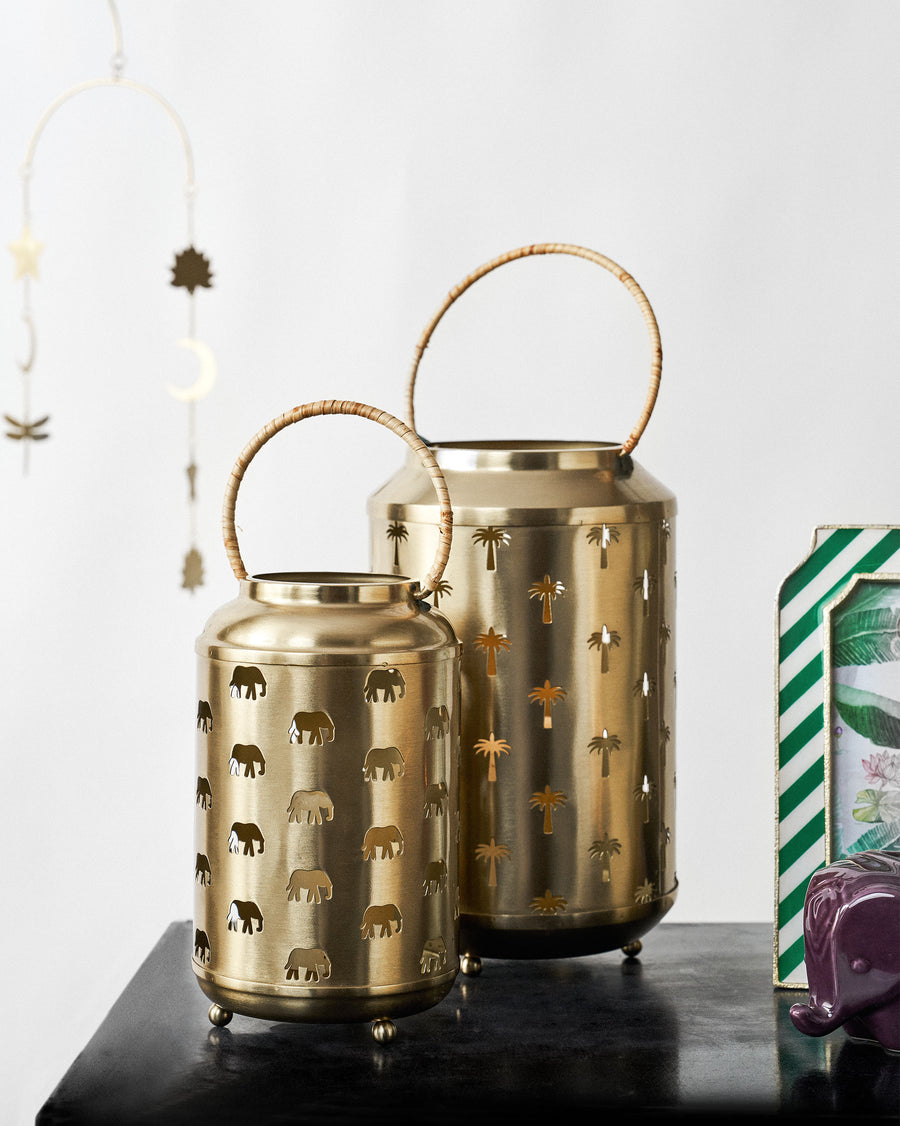 Two gold lanterns with rattan handles on a dark table under a hanging charm