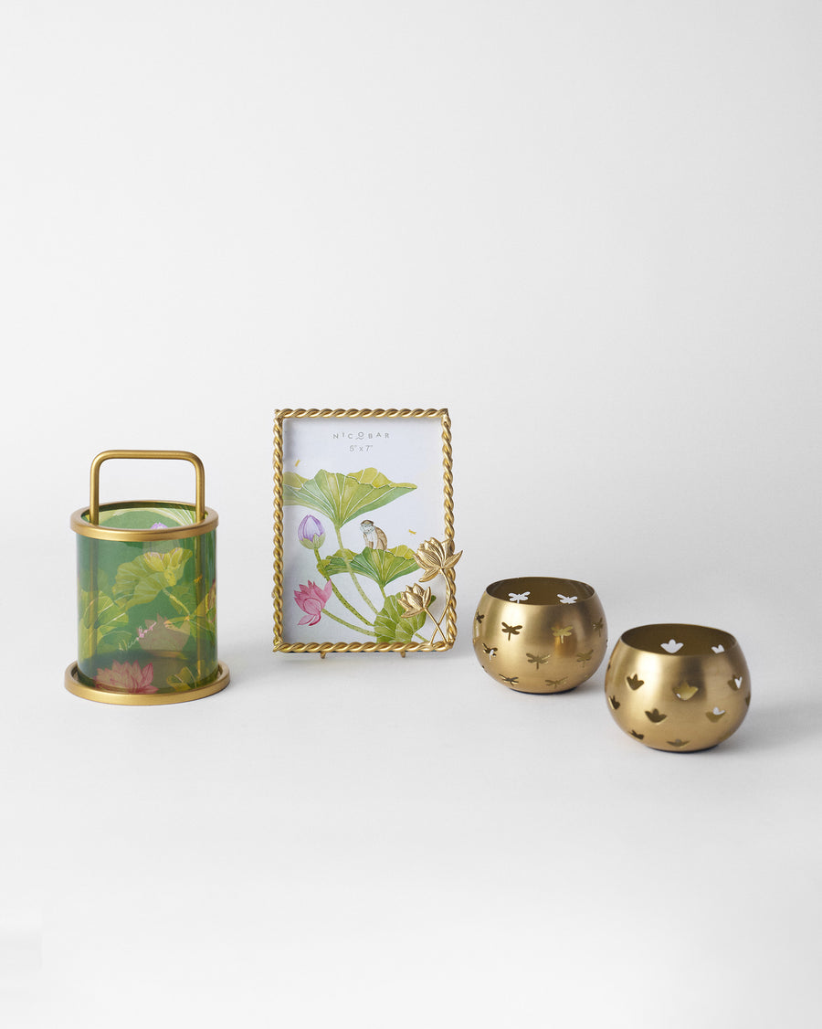 A green glass lantern, a gold photo frame and two cut-out votives in a row
