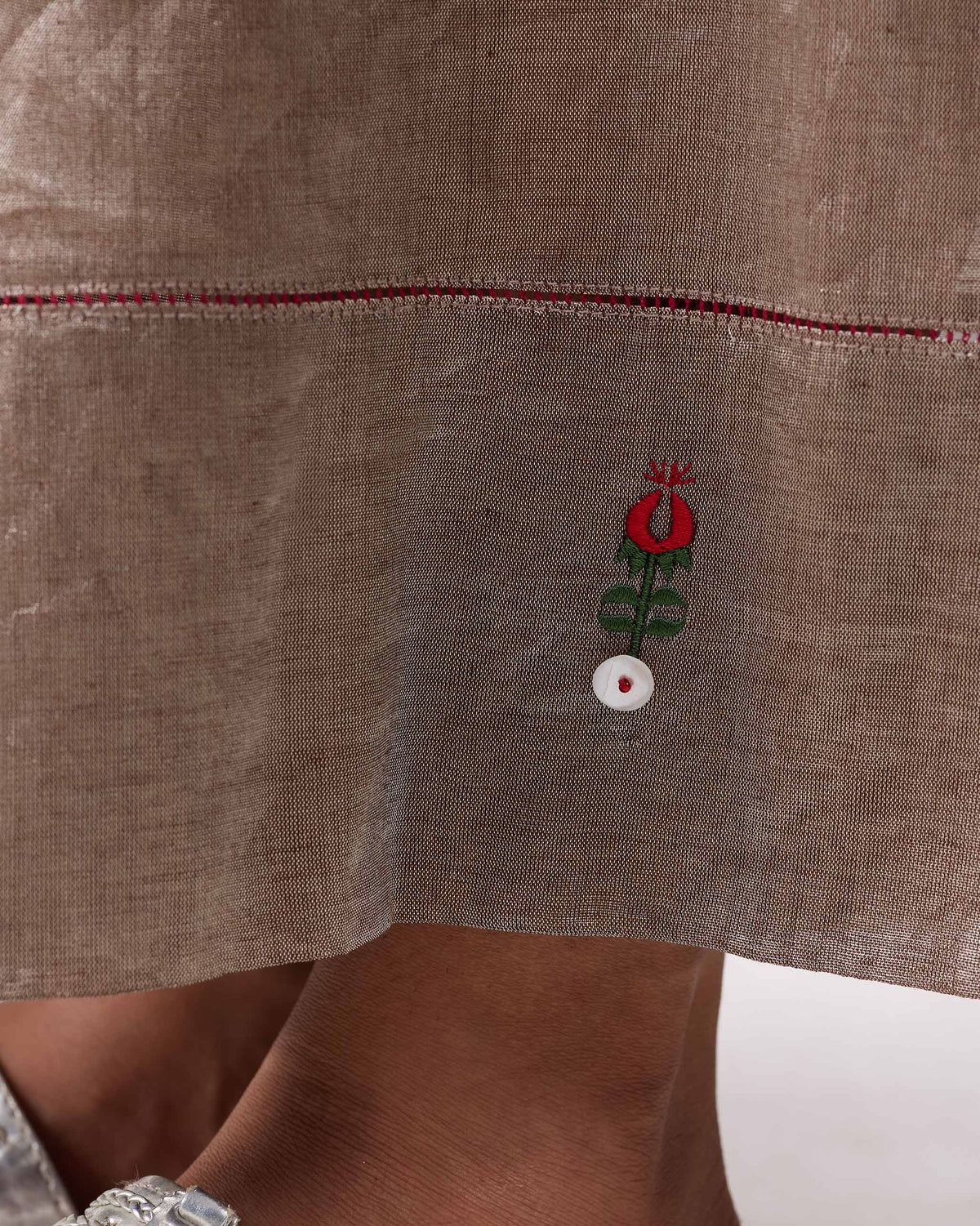 Close-up of silver Charisma pants hem with red stitch and floral motif.