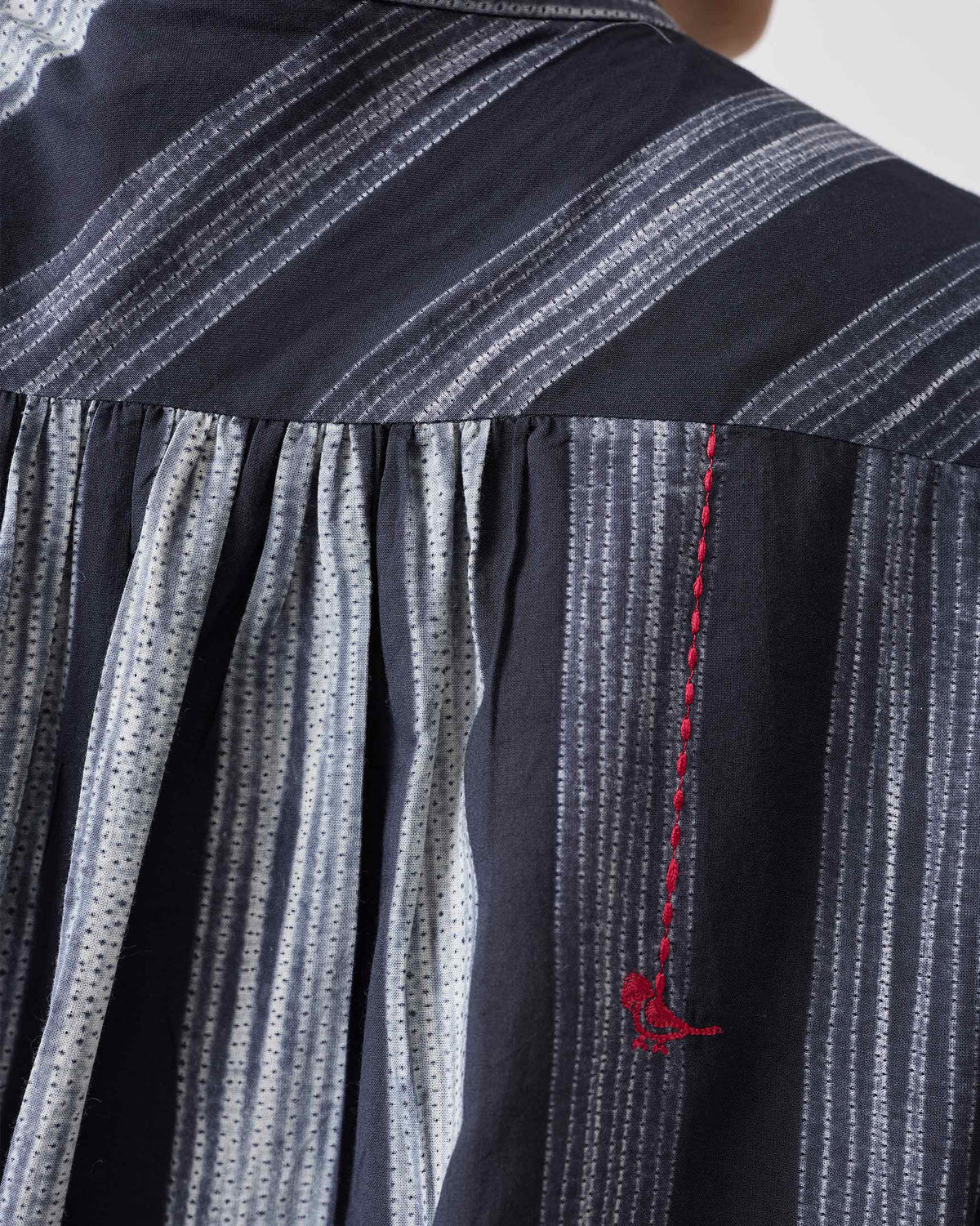 Close-up of the back yoke on a charcoal and ivory striped mandarin collar top with a red bird.