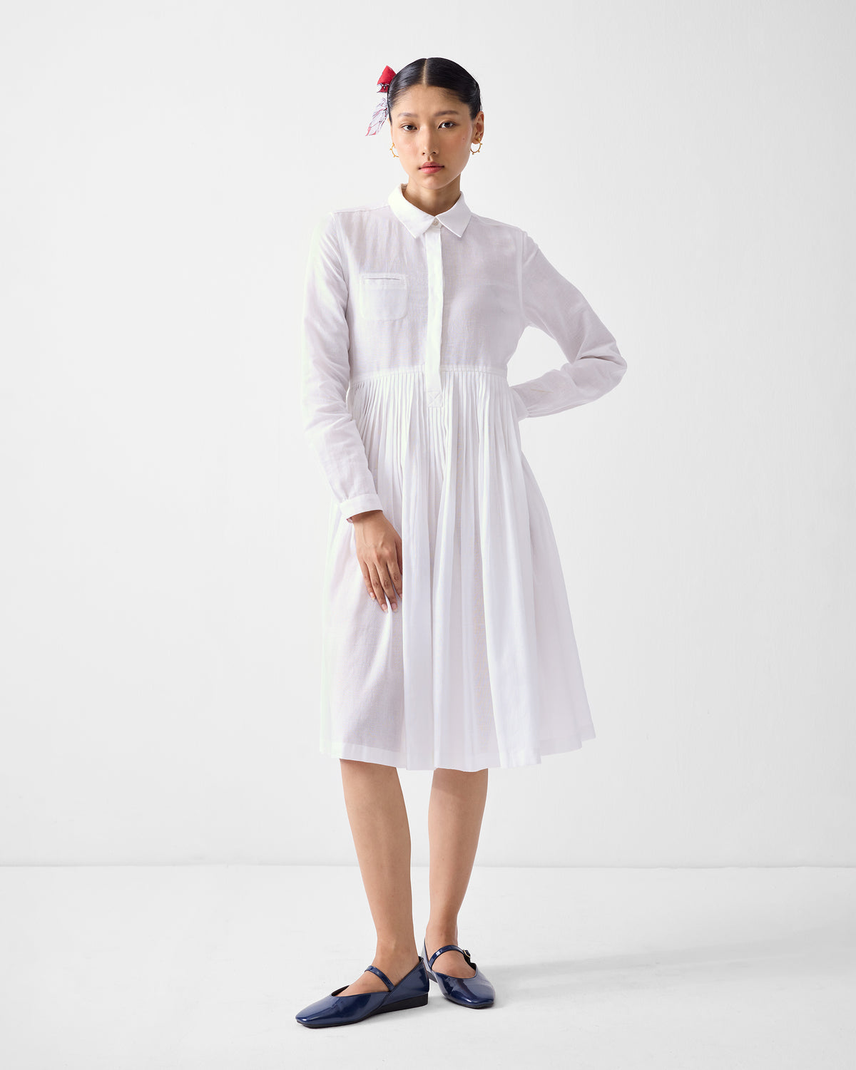 Person wearing a white Saviour shirt dress with a pleated midi skirt.