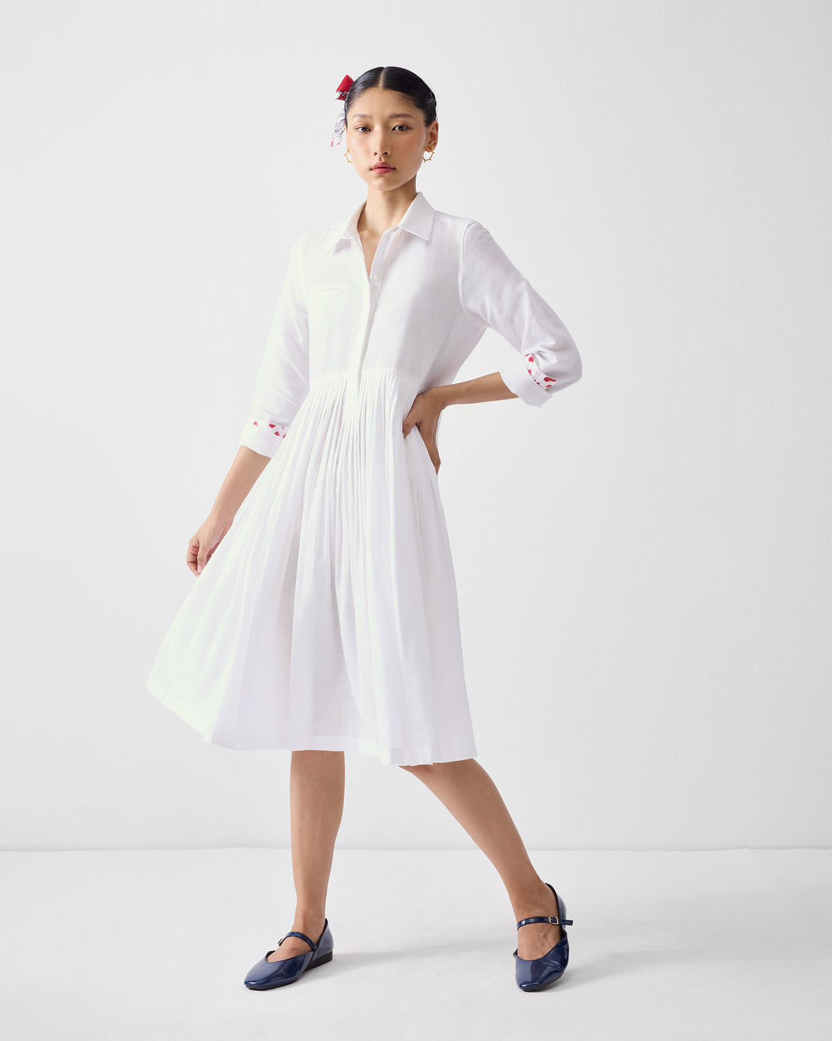 Person wearing a white shirt dress with red embroidery on the cuffs.