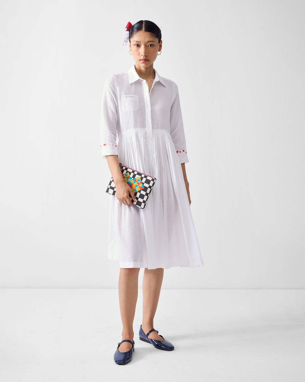 Person wearing a white shirt dress with embroidered cuffs and a pleated skirt.
