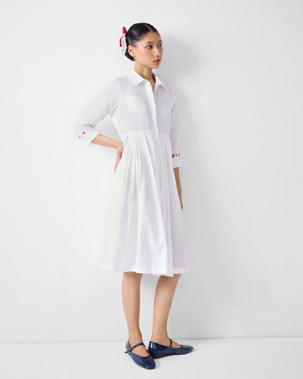 Person wearing a white collared shirt dress with a knee-length pleated skirt.