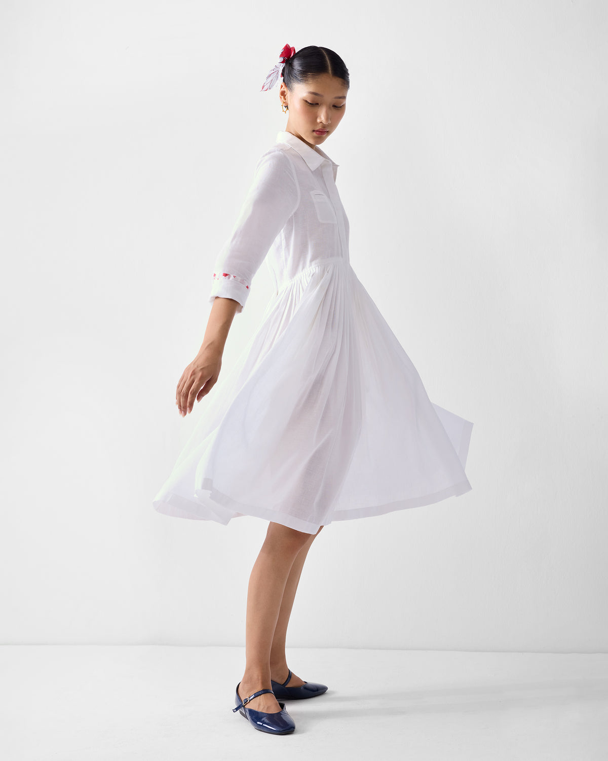 Side view of a white shirt dress with a flared pleated skirt in motion.