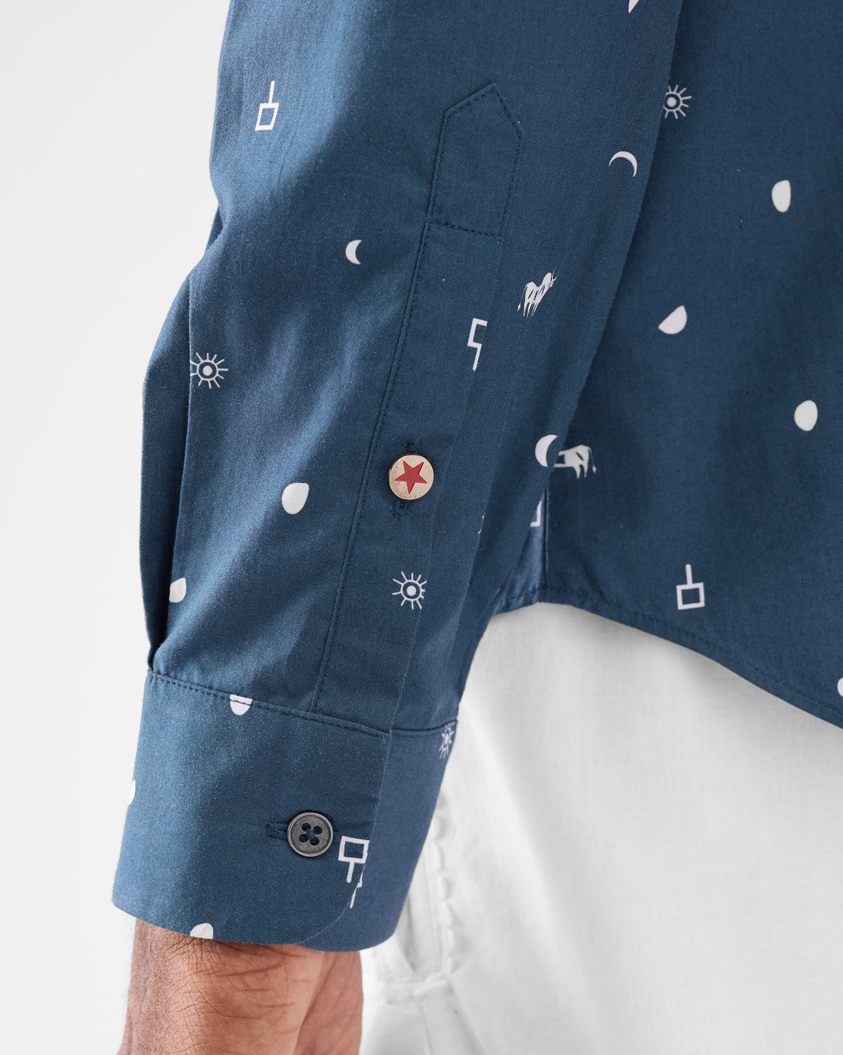 Close-up of a navy Hakuna shirt sleeve with a red star button on the placket.
