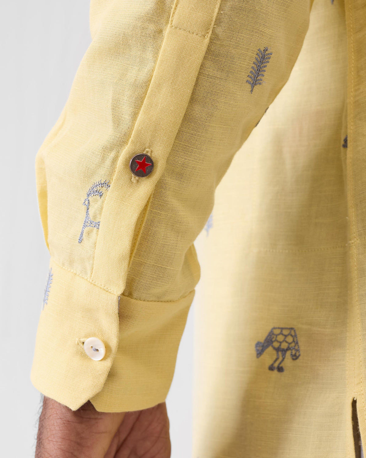 Close-up of a light yellow Astral kurta sleeve with grey embroidery and a red star button.