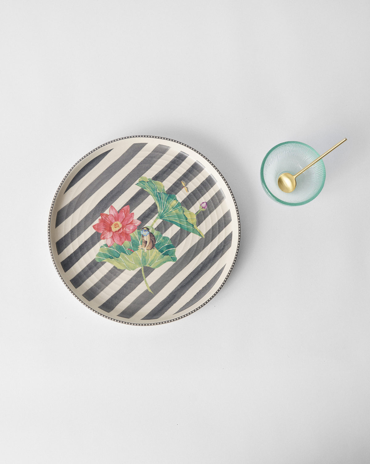 Lily Pond platter with lotus motif beside a green glass bowl and gold spoon.
