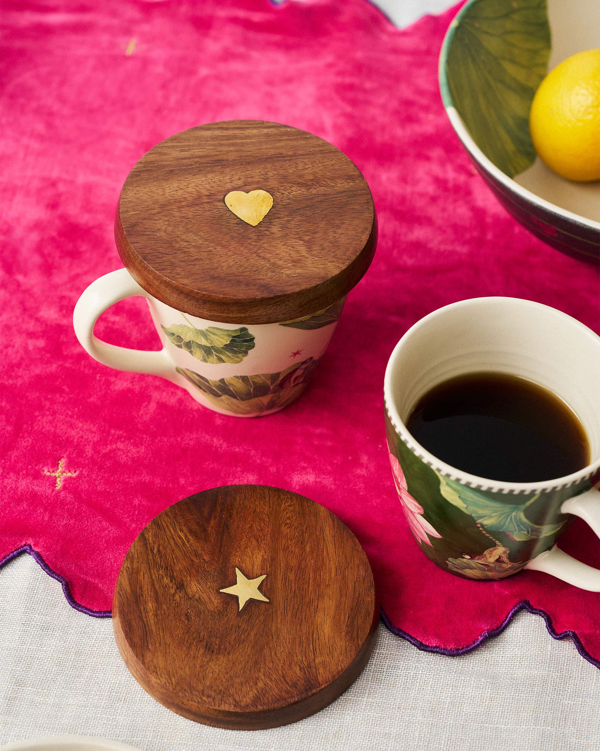 Wooden Aster mug lids with brass inlays used on floral mugs at a table.