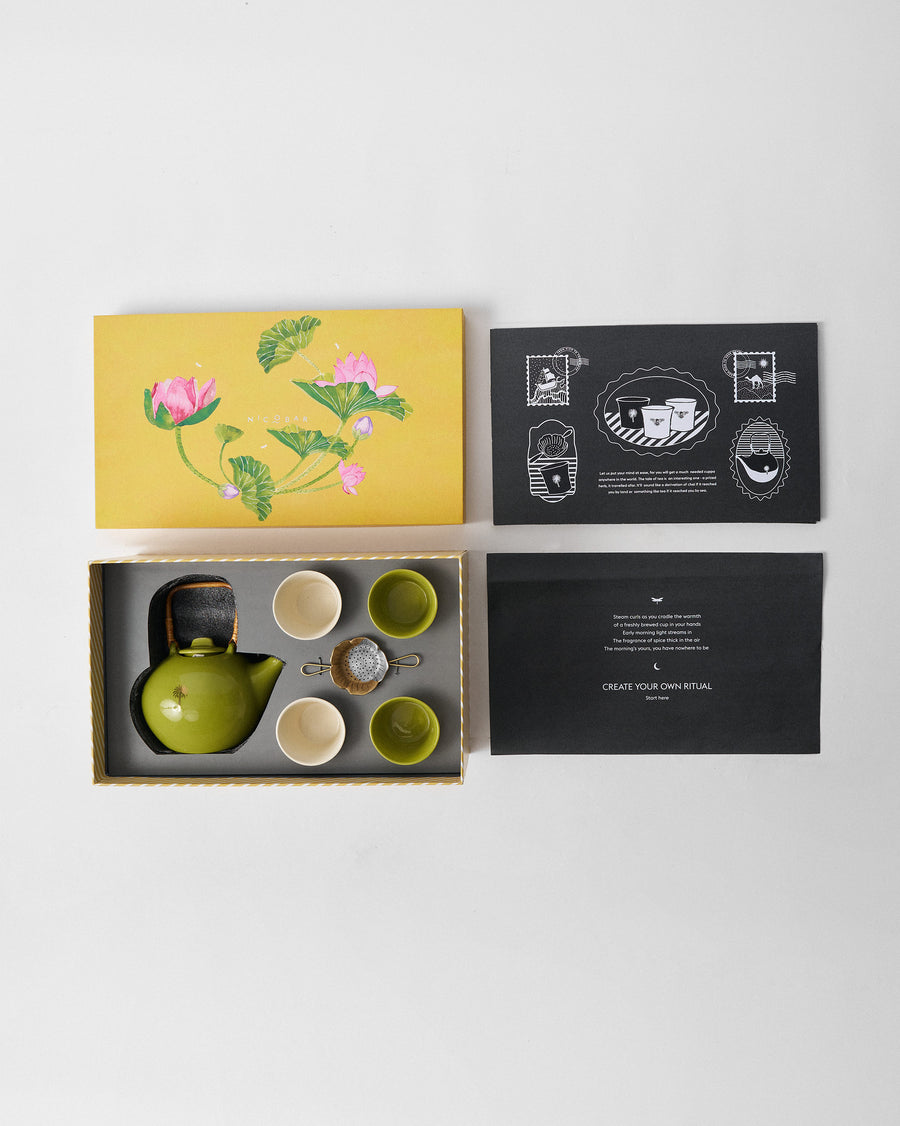 The tea set packed in its box beside the yellow lotus lid and cards