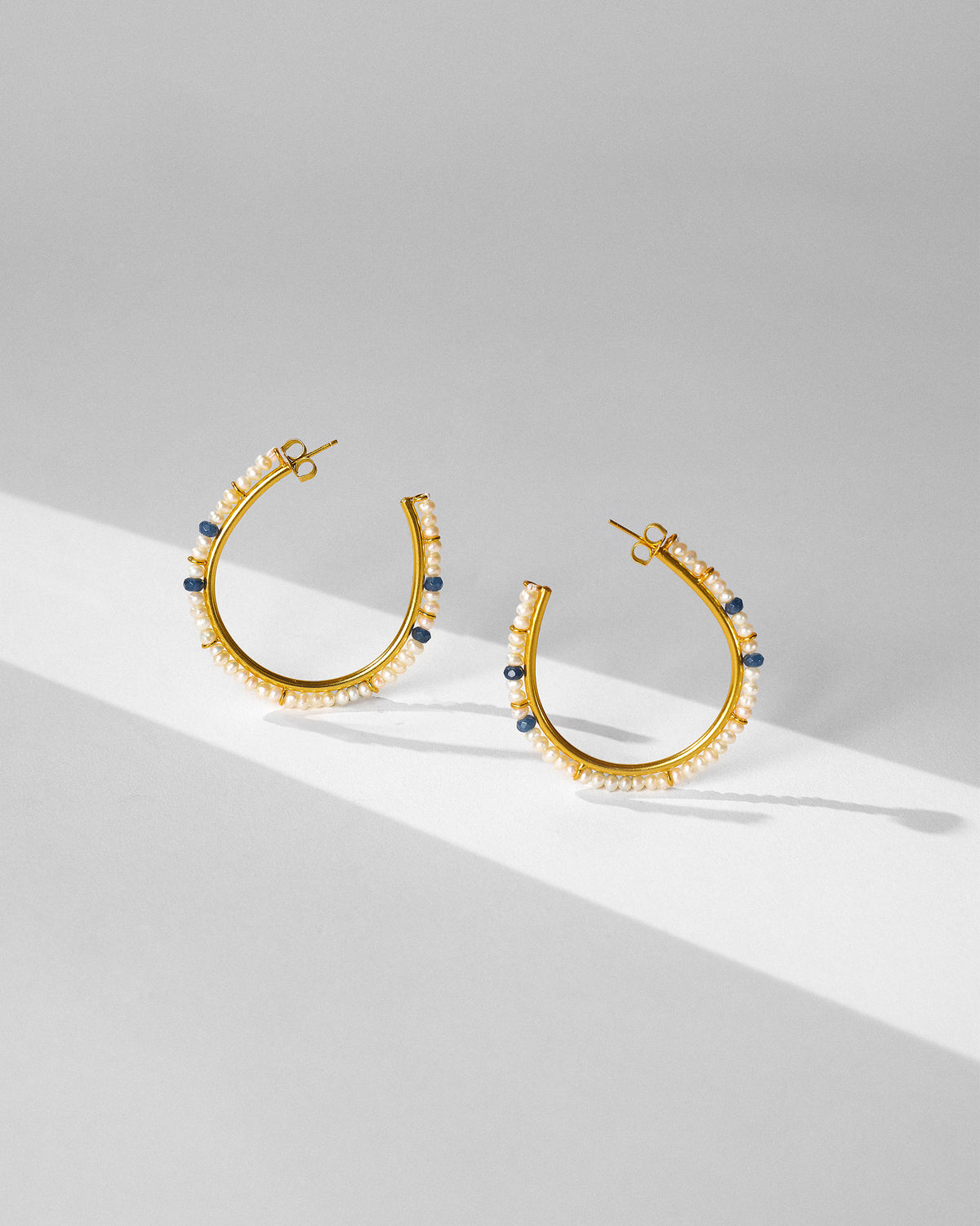 Pair of large gold Raja balis with pearls and blue beads laid flat.
