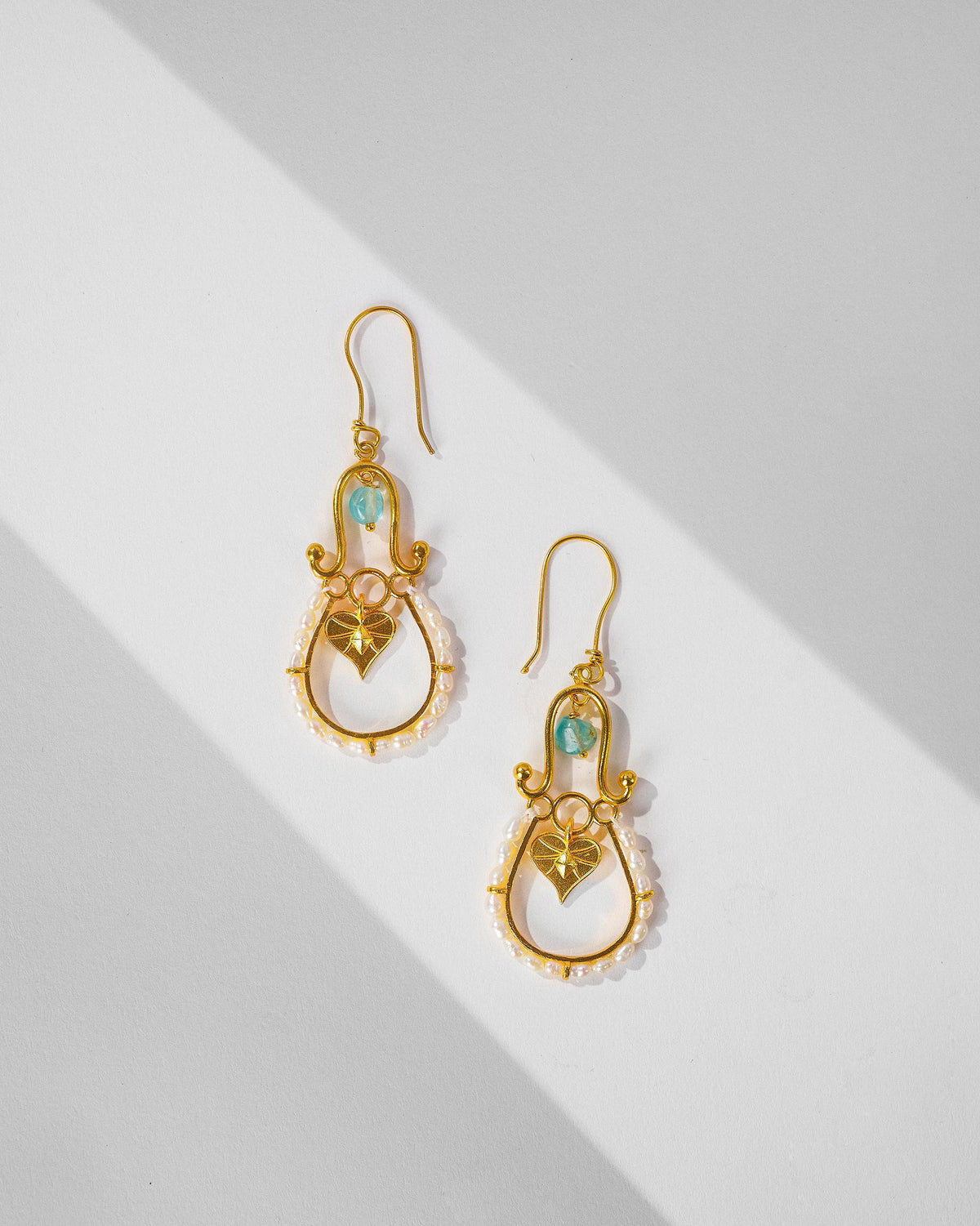 Pair of gold Peepal Patta danglers with pearls and leaf charms laid flat.