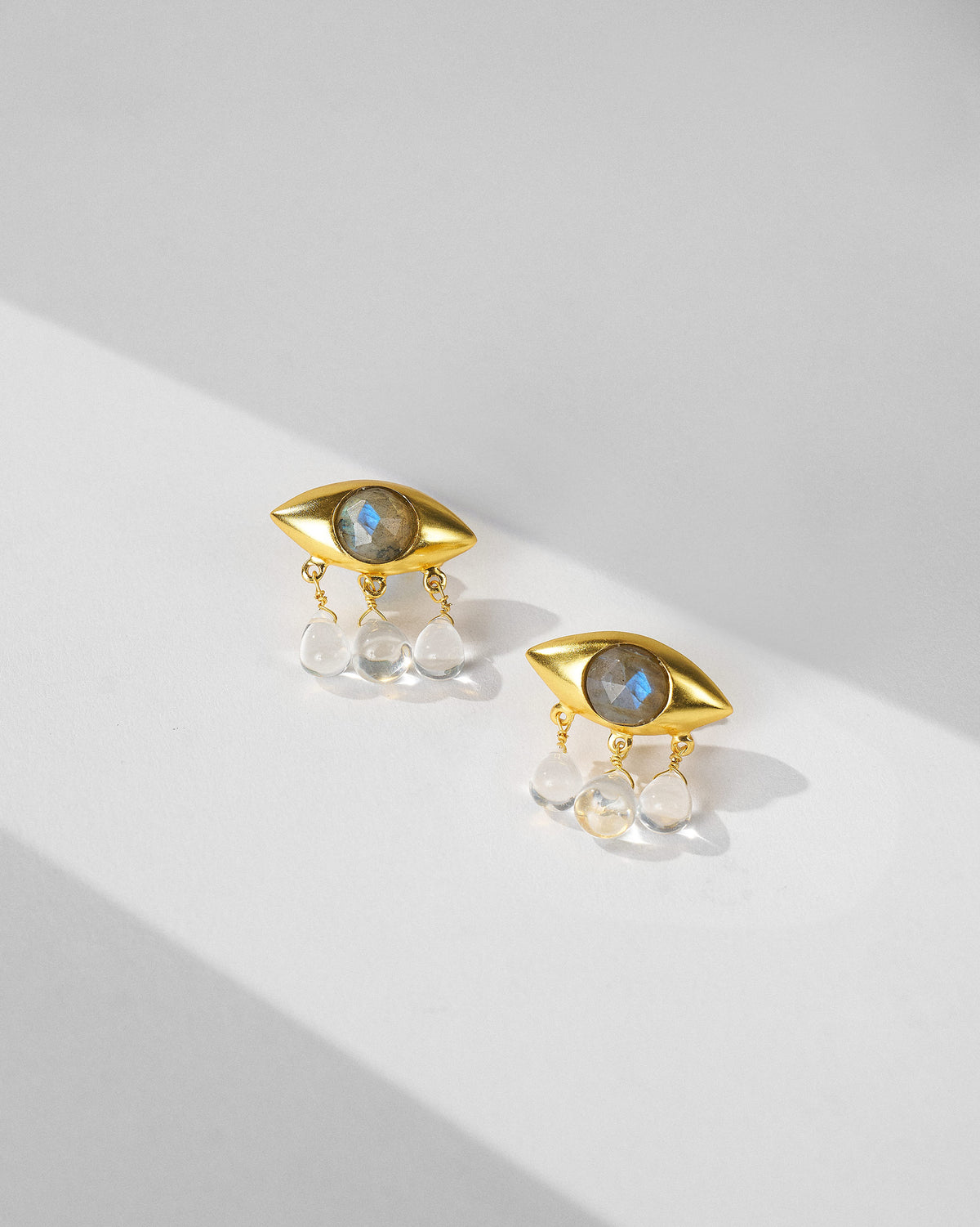 Pair of gold Noor eye earrings with labradorite and quartz drops laid flat.