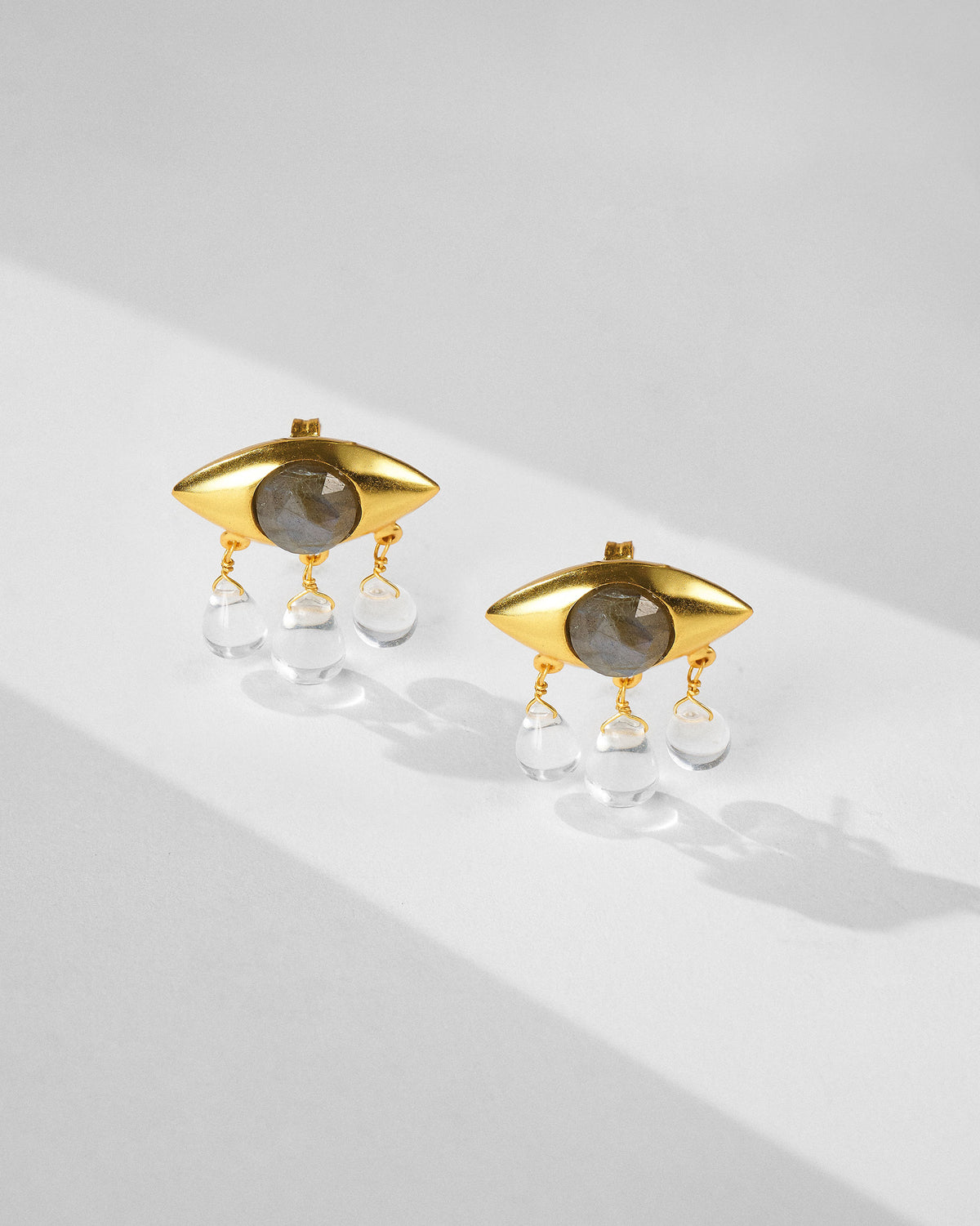 Pair of gold Noor eye earrings with clear quartz drops.