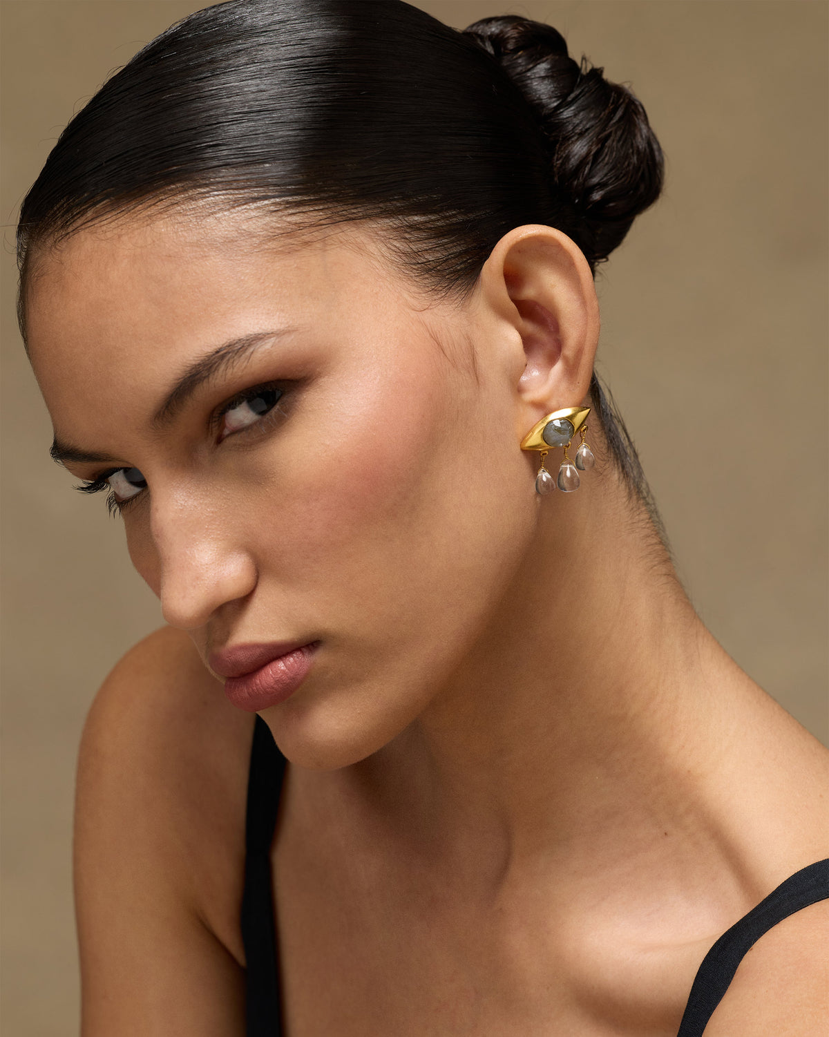 Person wearing gold Noor eye earrings with labradorite and quartz drops.