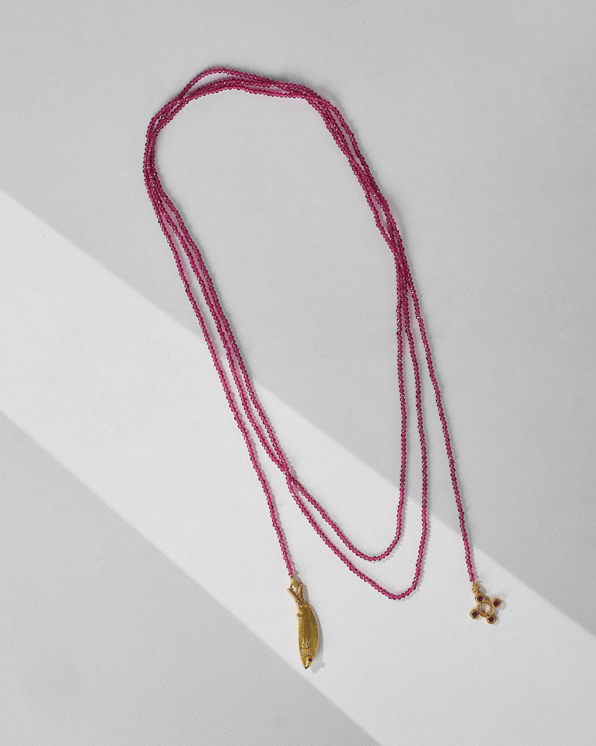 Long Jal Pari magenta bead strand with gold fish and circular charms laid flat.