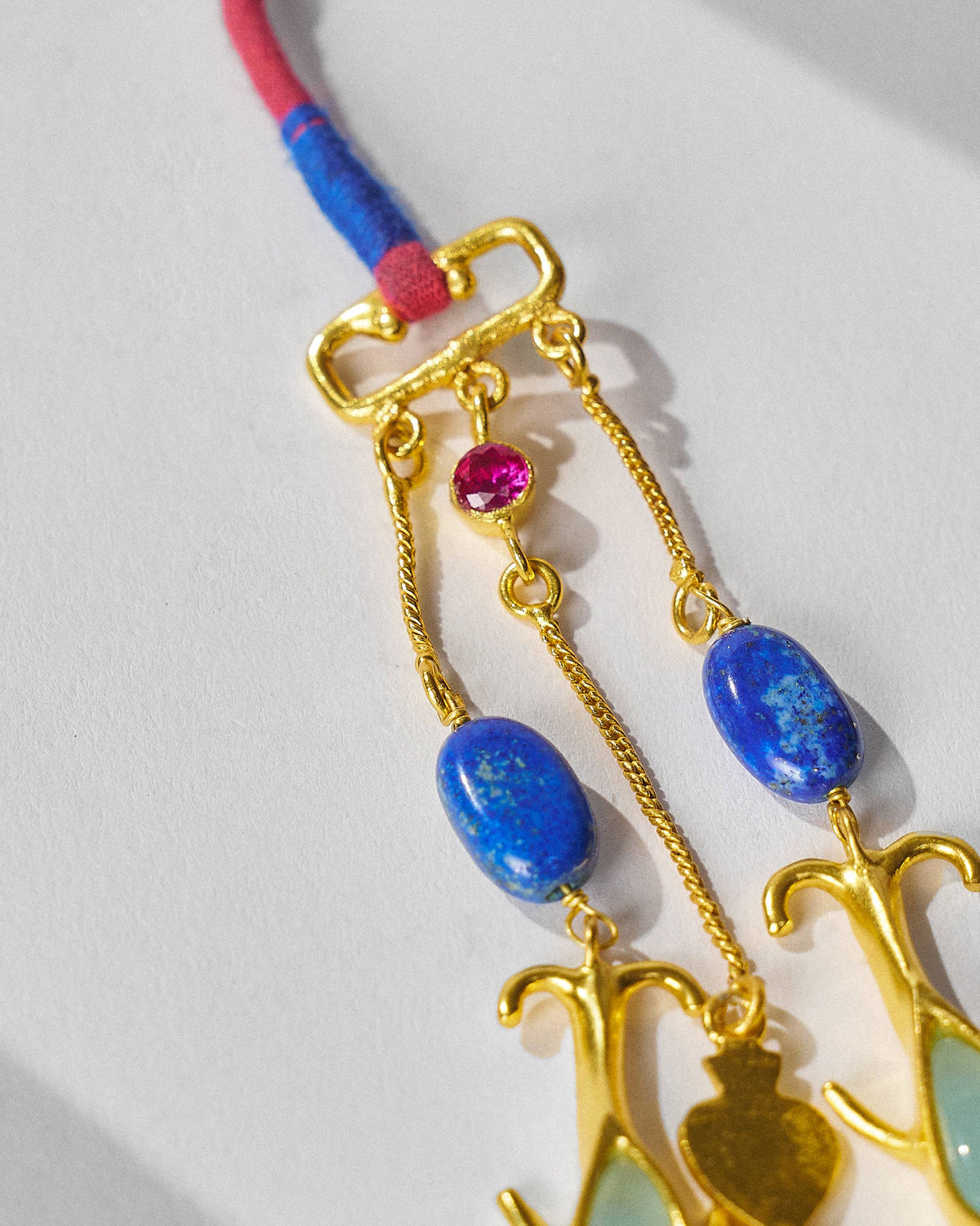 Close-up of Indus necklace drops with lapis stones and gold charms on a red cord.