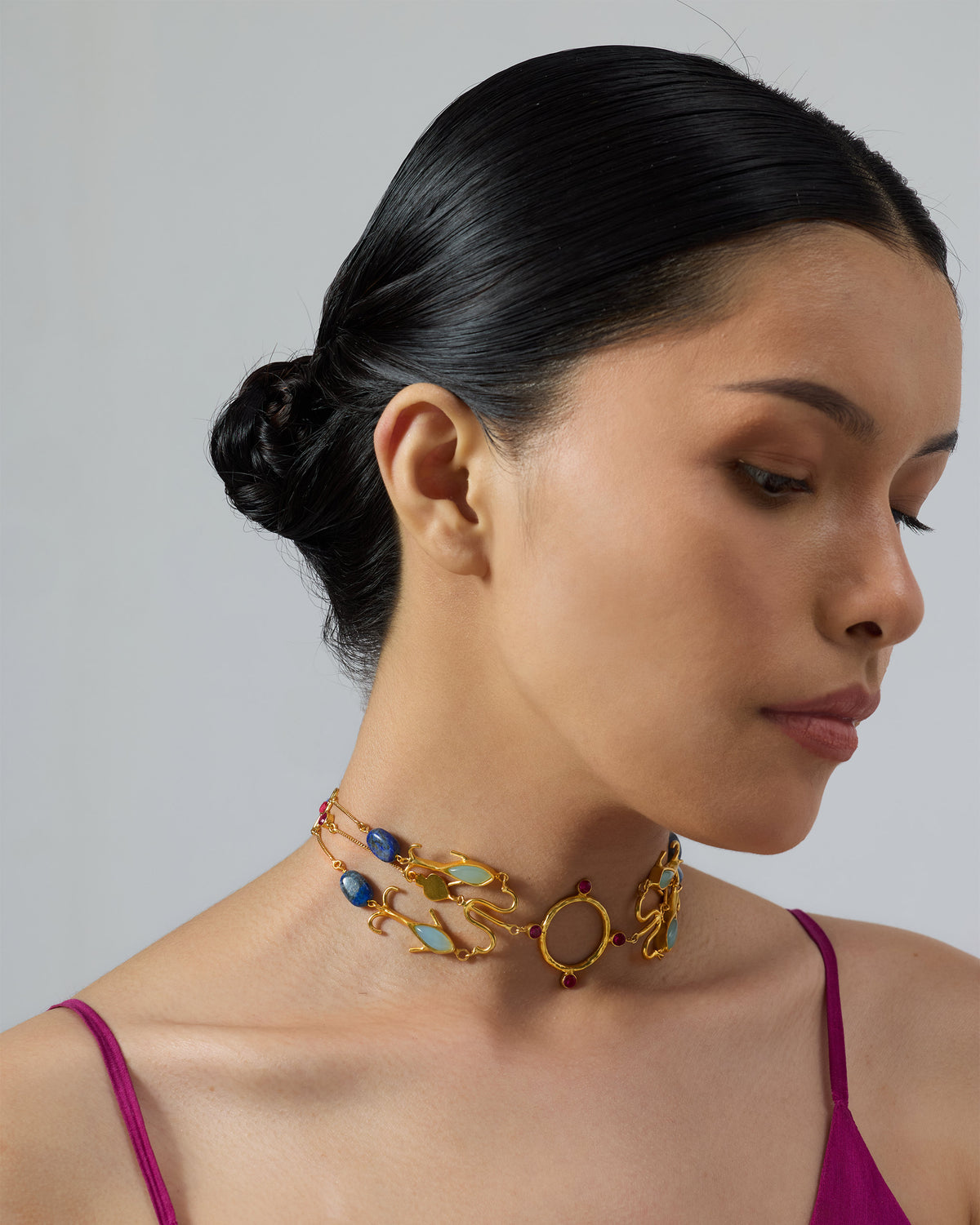 Side profile of a gold Indus necklace with blue and green stones on a person.