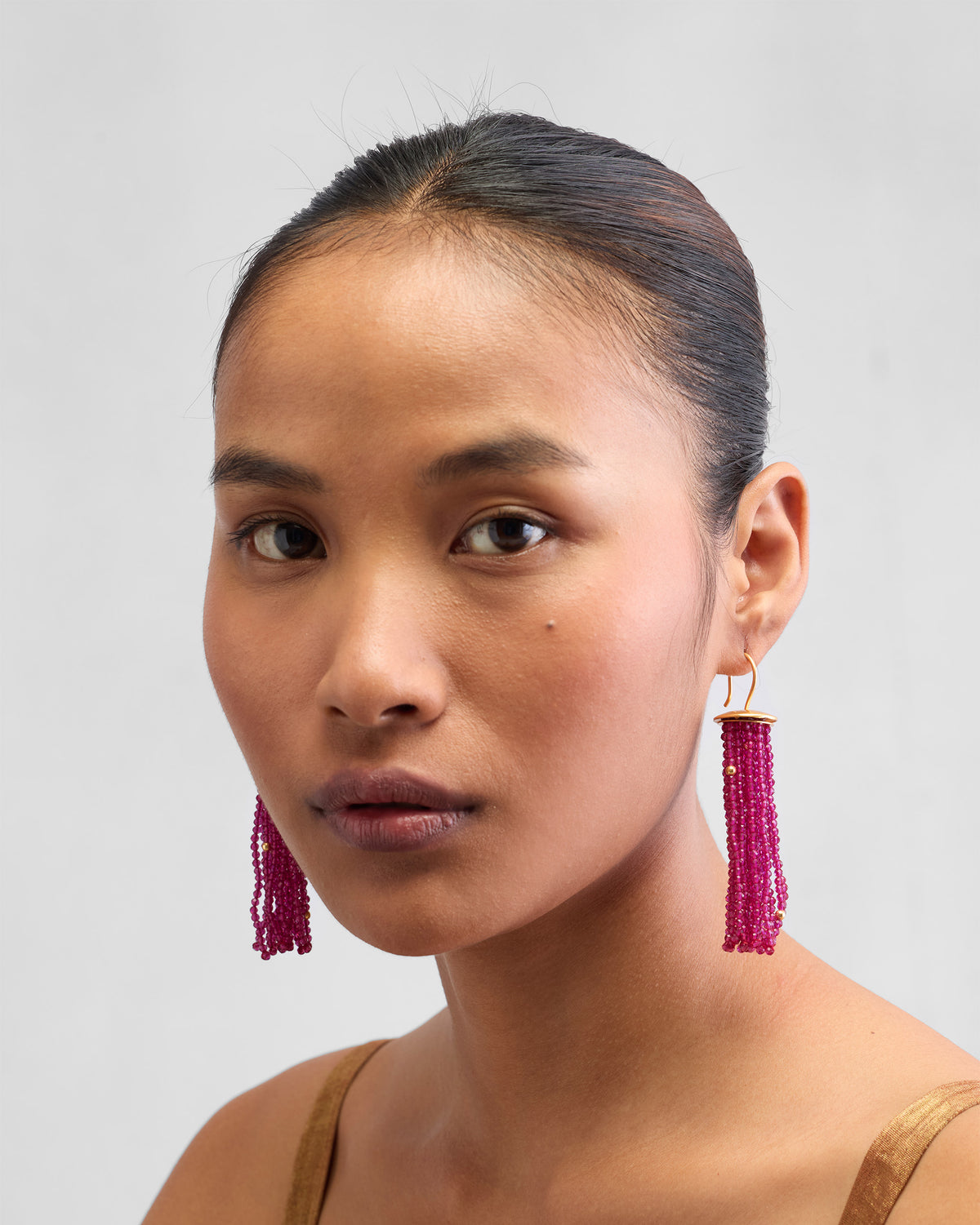 Person wearing long magenta Glass Tassel earrings with gold caps.