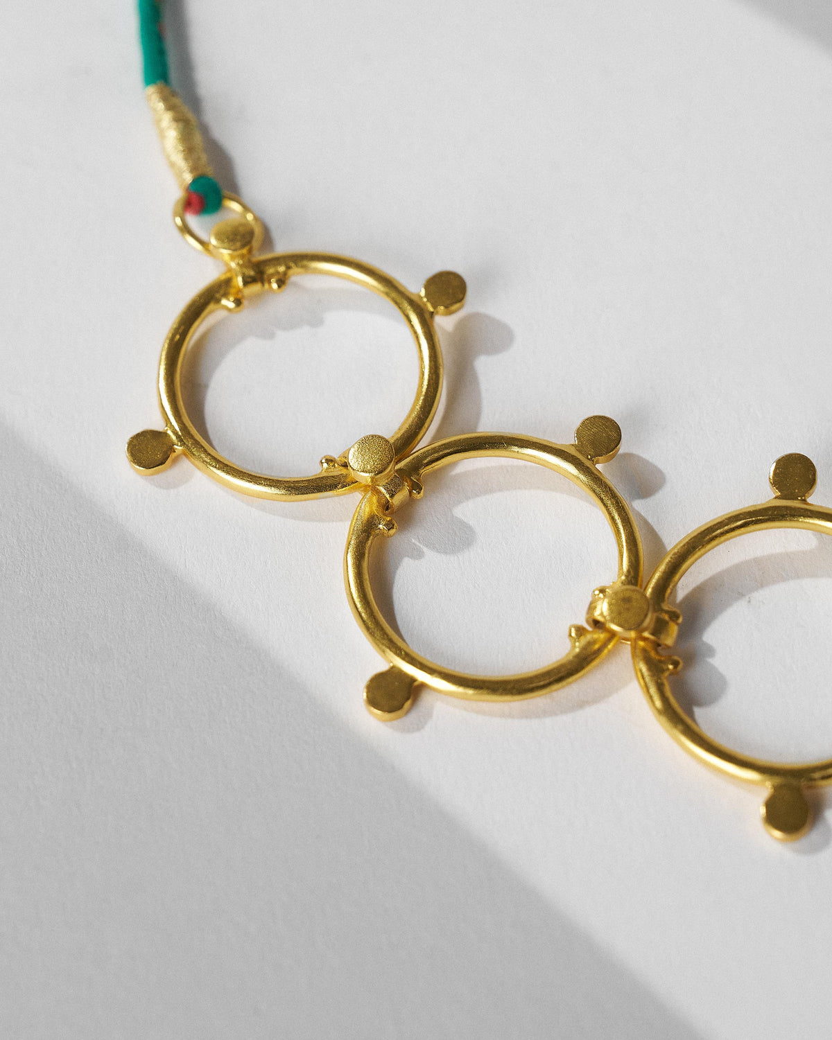 Close-up of linked gold circles joining a teal cord on a Panch Circle necklace.