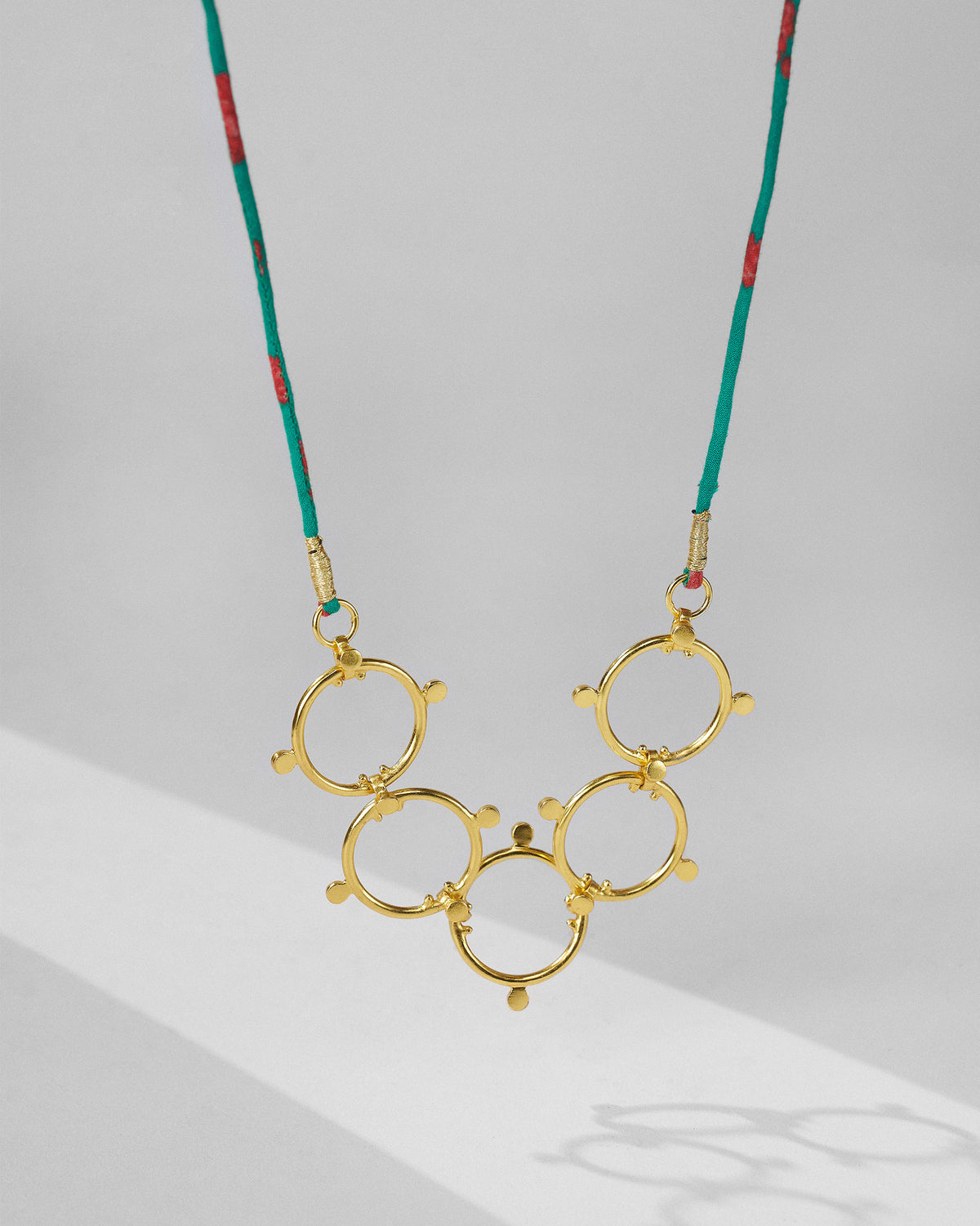 Panch Circle necklace with five linked gold circles on a teal cord.
