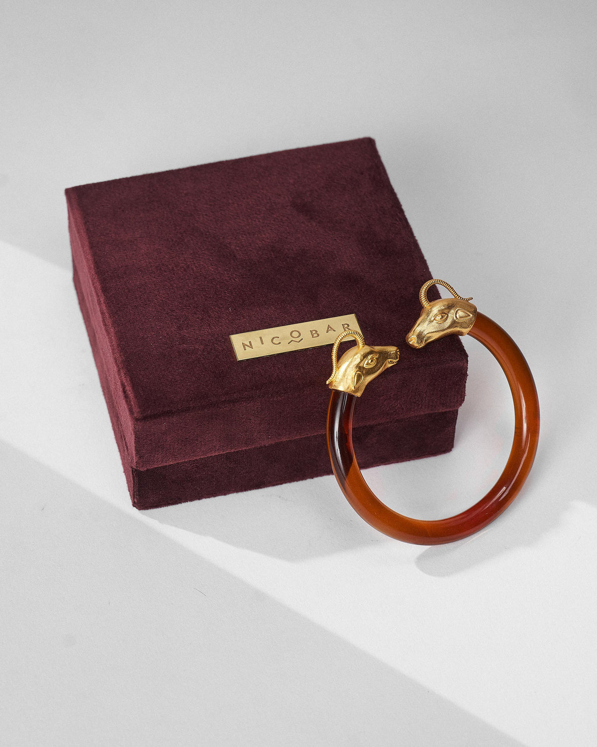 Amber Unicorn bangle resting on a burgundy Nicobar velvet gift box.