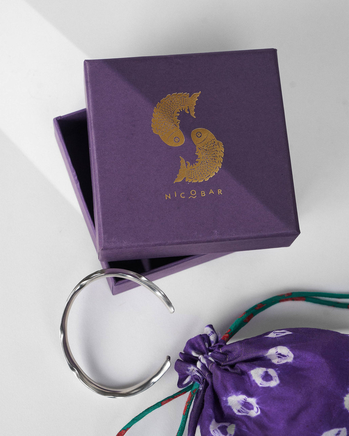 Thin silver Batur bangle with a purple Nicobar gift box and pouch.