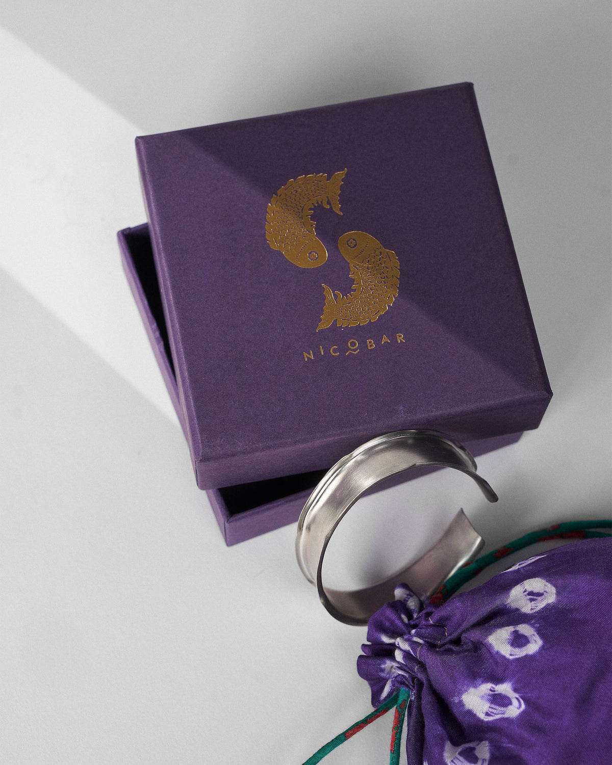 Thick silver Batur bangle with a purple Nicobar gift box and pouch.