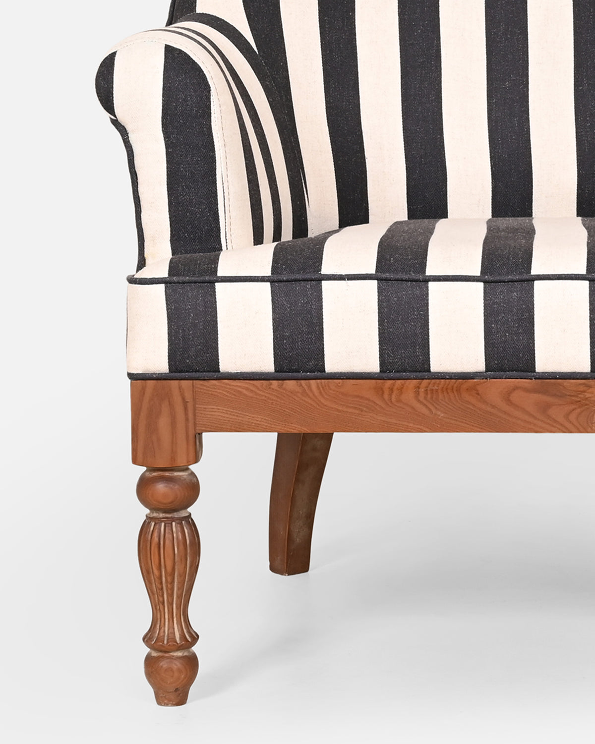 Close-up of Cove Arm Chair showing striped upholstery and a fluted wooden leg.