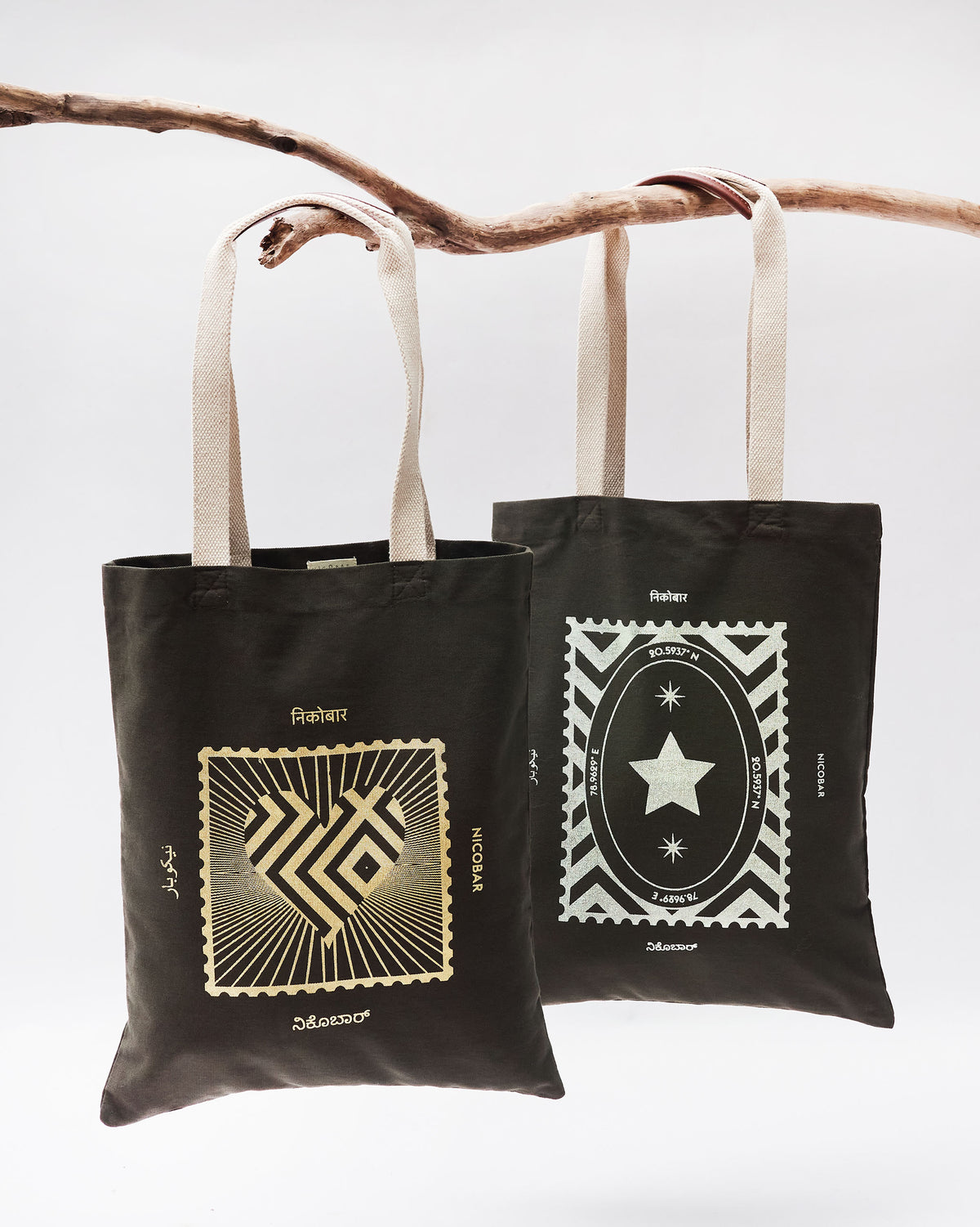 Two charcoal Decade Totes hanging side by side with gold and silver stamp prints.