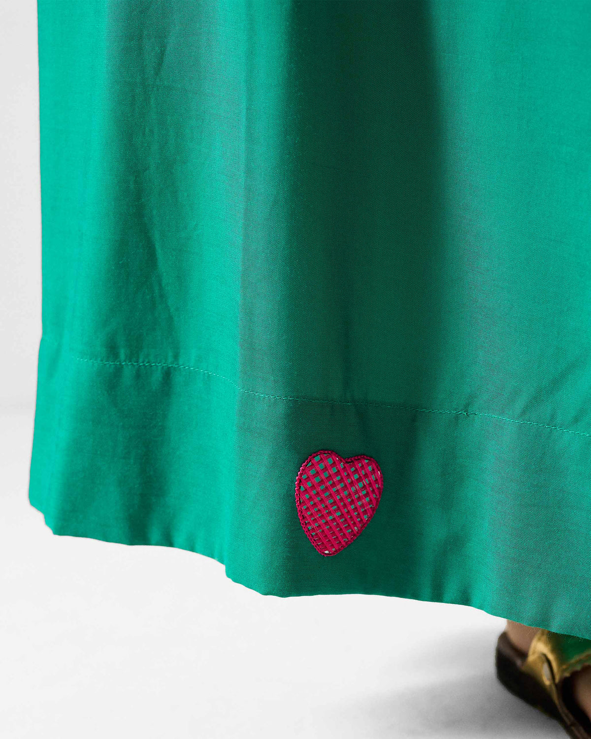 Close-up of a red heart appliqué on the hem of green paperbag pants.