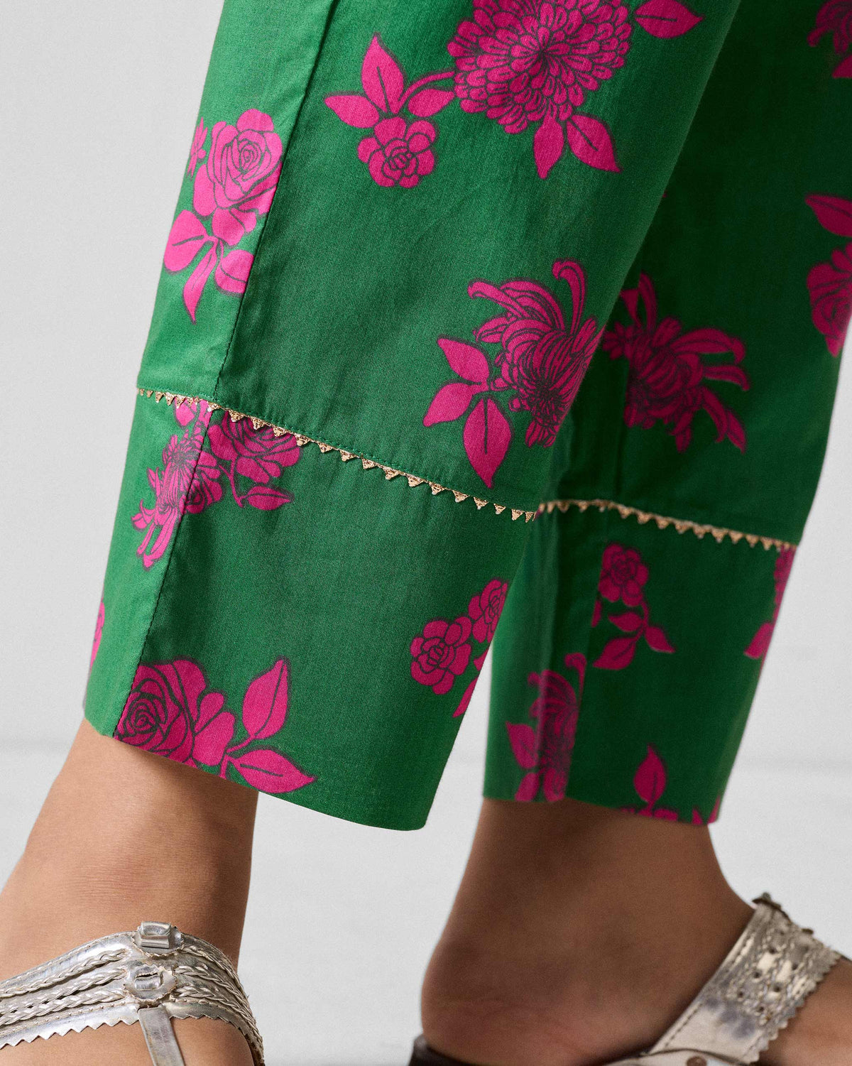 Close-up of the gold trim and pink florals near the hem of green Novel narrow pants.
