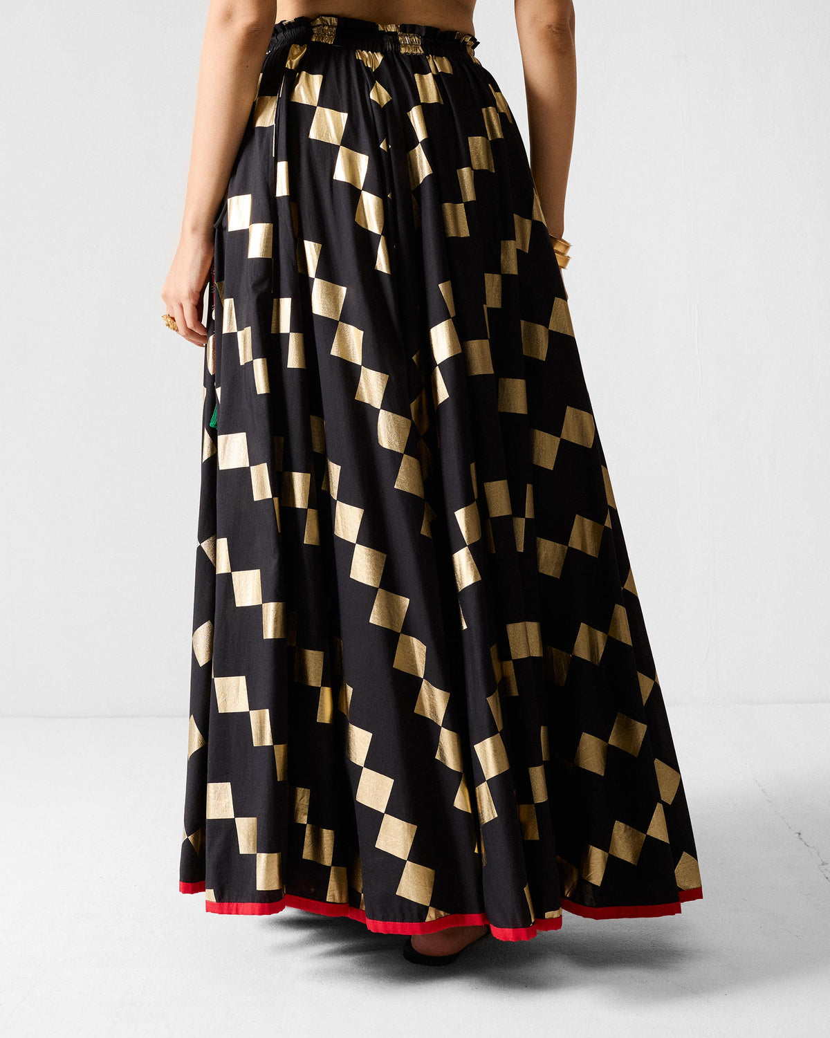 Back of a black Afsar Skirt with gold foil squares and a red hem.