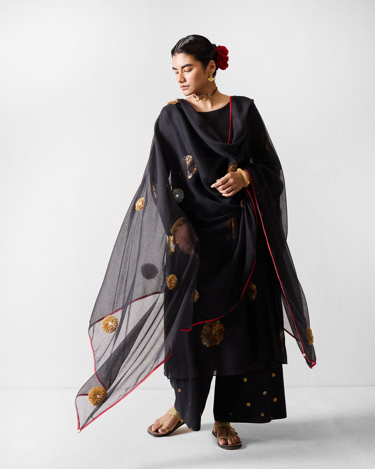 Person wearing a black and gold boat-neck kurta with a sheer black dupatta.