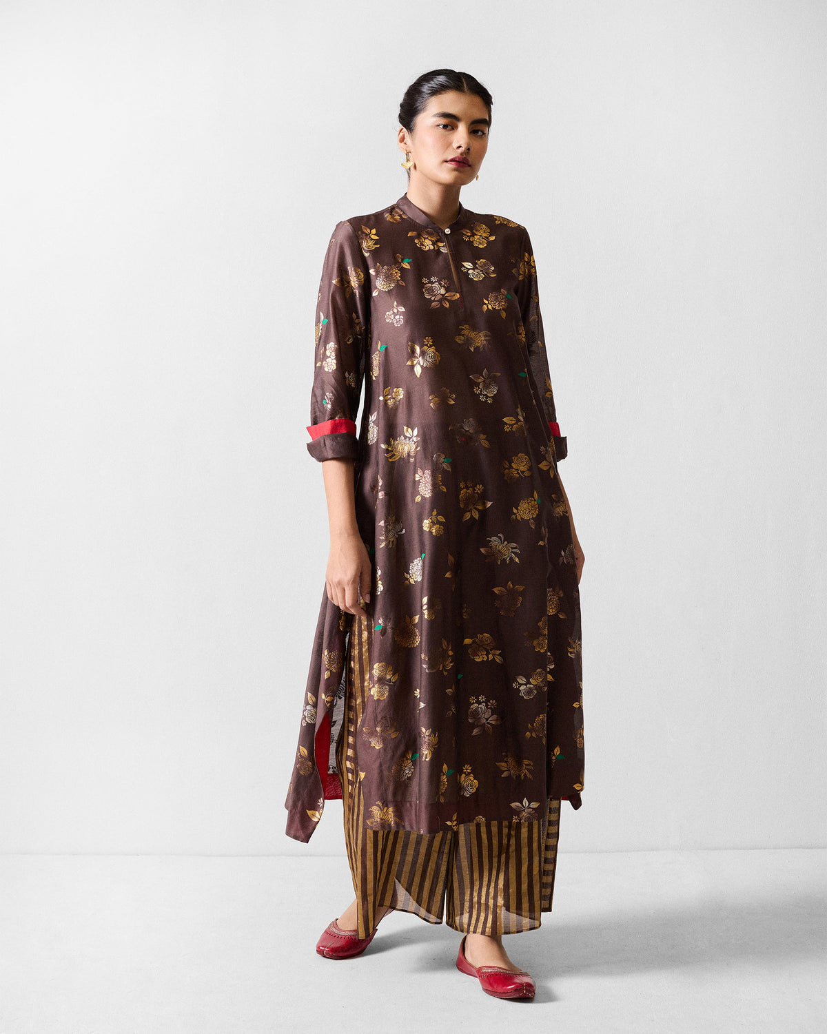 Person wearing a brown gold-print kurta with red cuff lining.