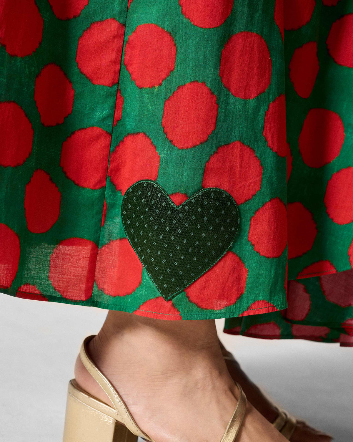 Close-up of a heart patch near the hem of a green polka-dot dress.