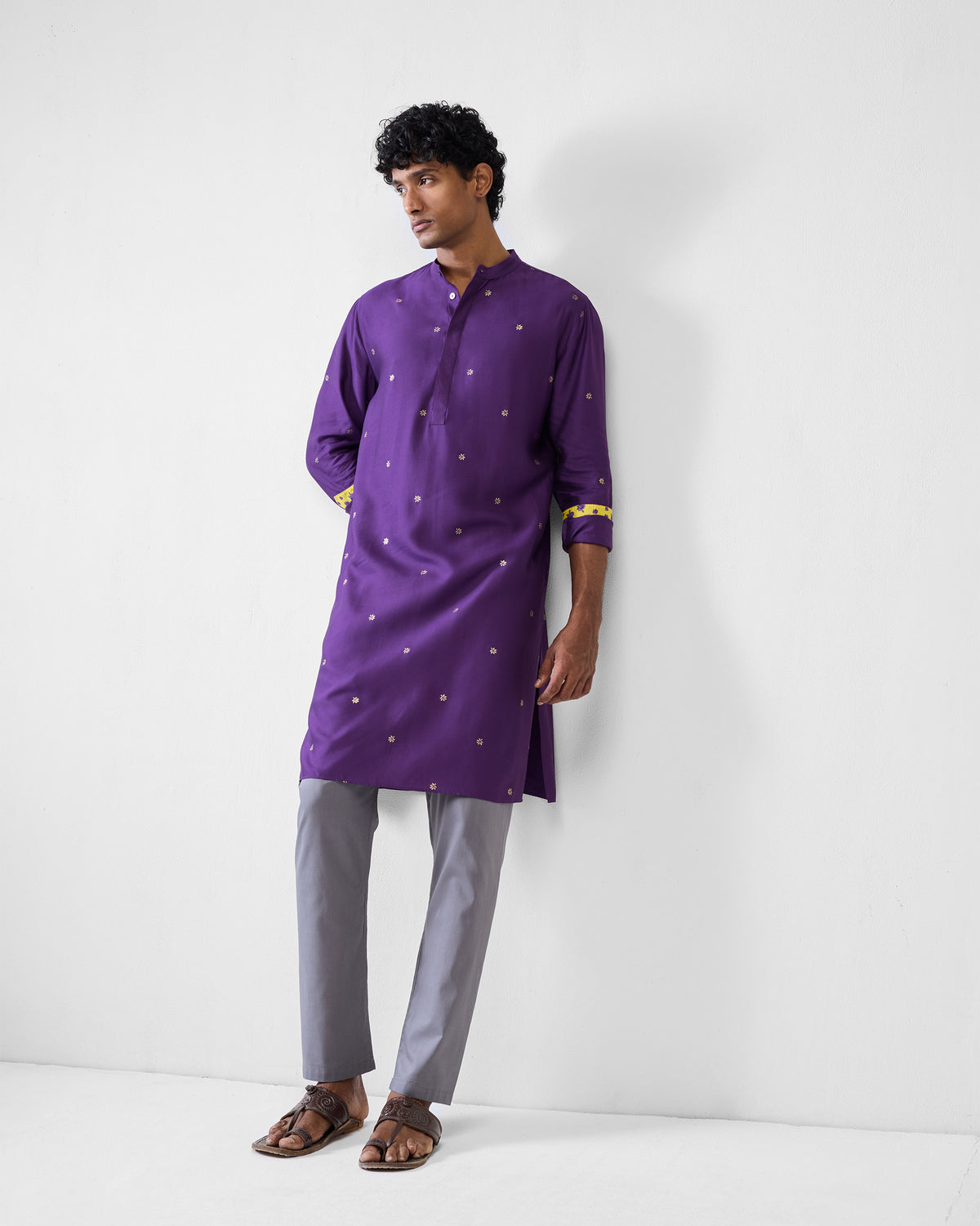 Person wearing a purple Neckband Kurta with gold buta and yellow cuff lining.