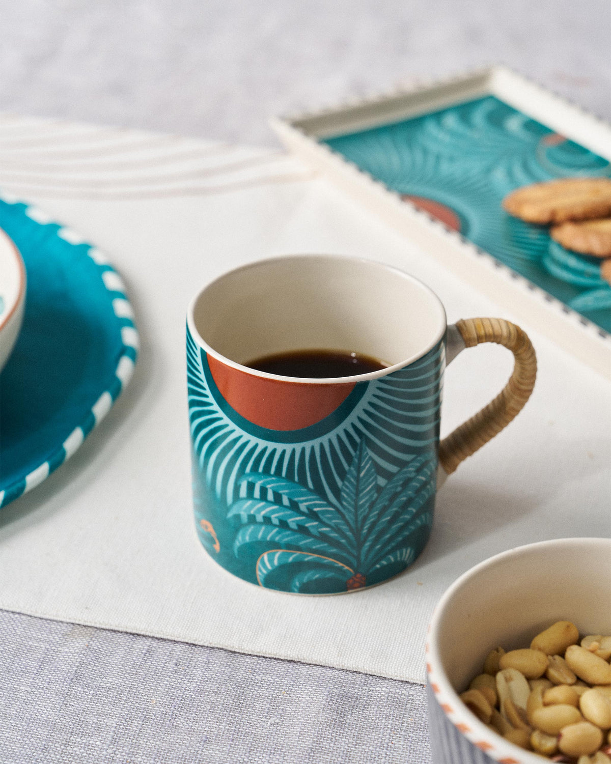 The Caden mug with coffee beside a teal tray and nuts.