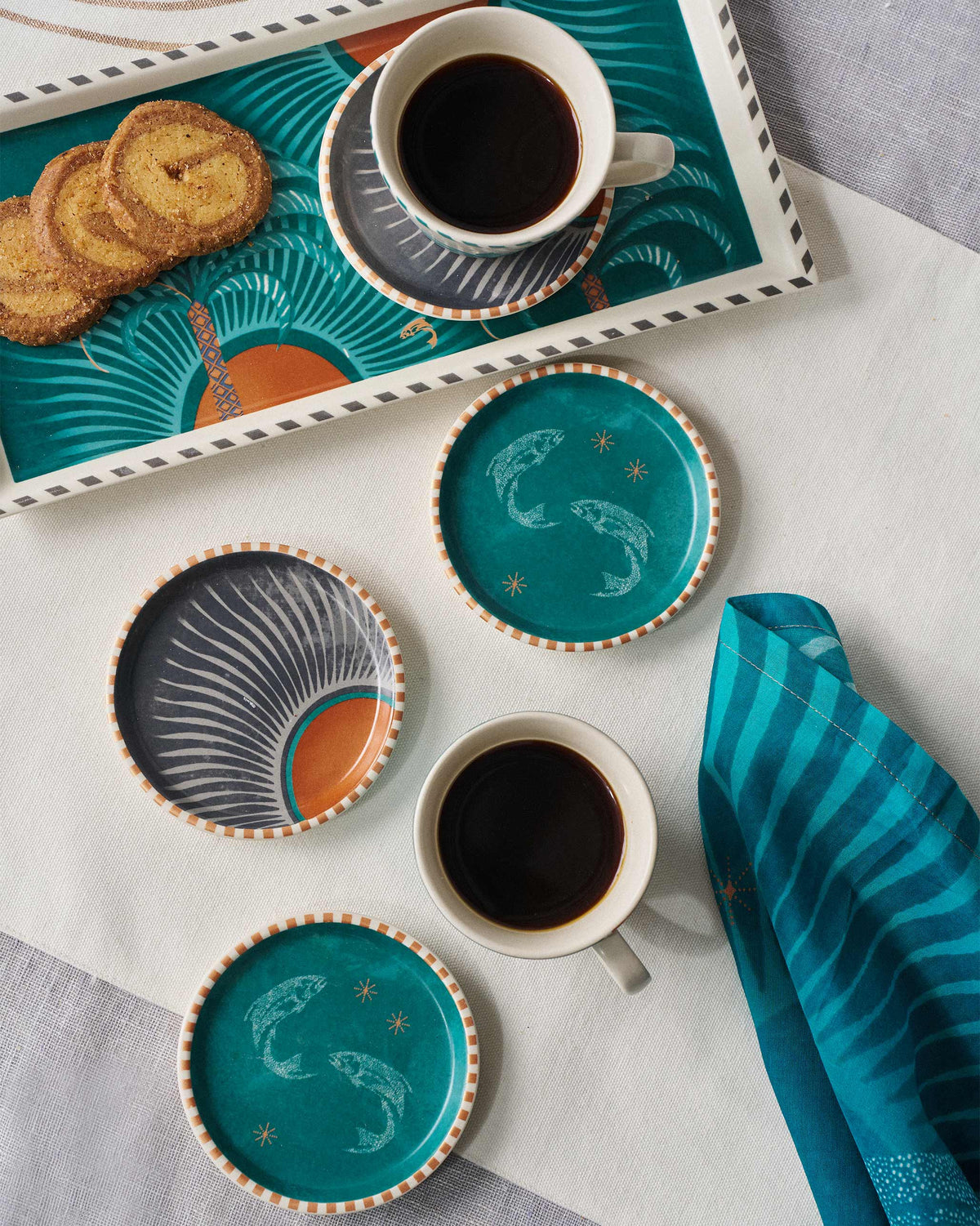 Aluna coasters under coffee mugs in a teal and charcoal table setting.