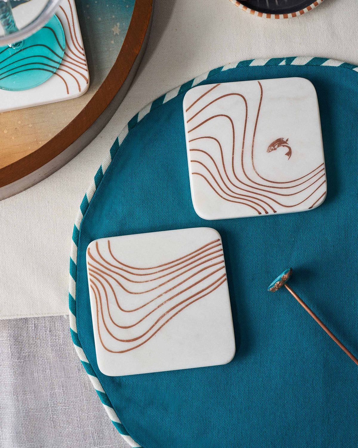 White marble Dusk coasters with copper waves, one showing a fish.