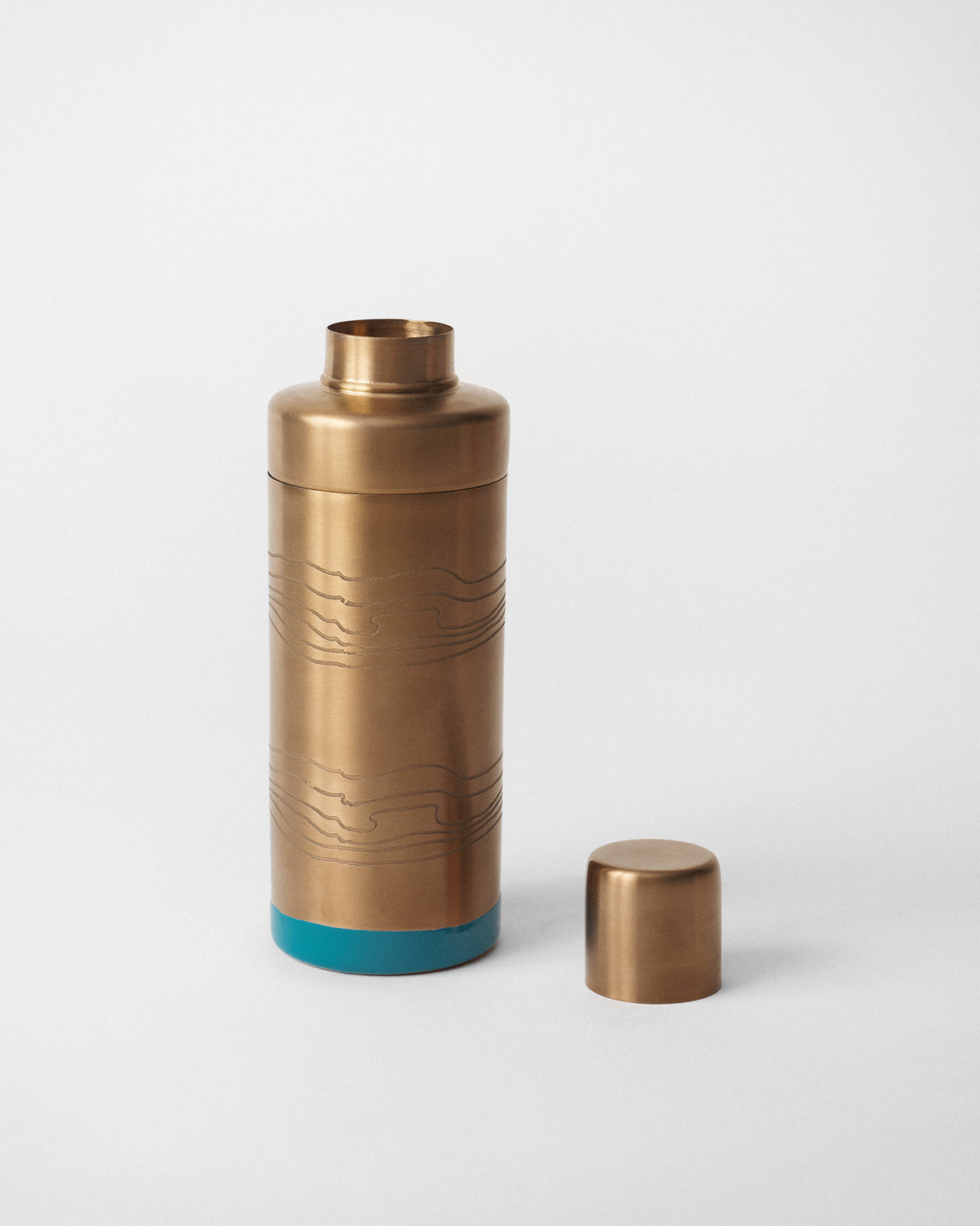 Brass cocktail shaker with its cap removed beside the teal-based body.