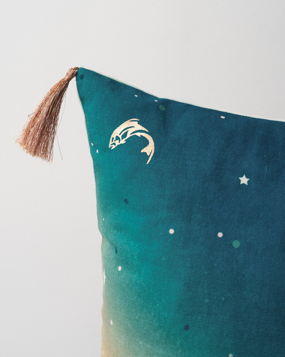 Close-up of Lumen Cushion Cover showing a gold fish motif and a tassel.