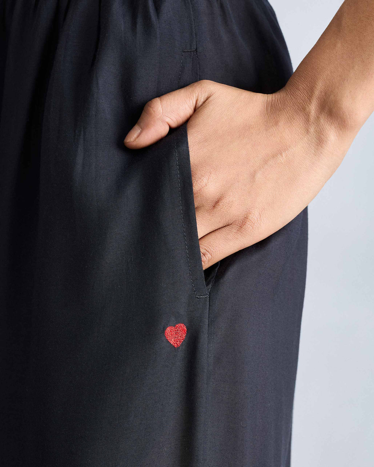 Close-up of black Classic Pyjama pants with a side pocket and red heart embroidery.