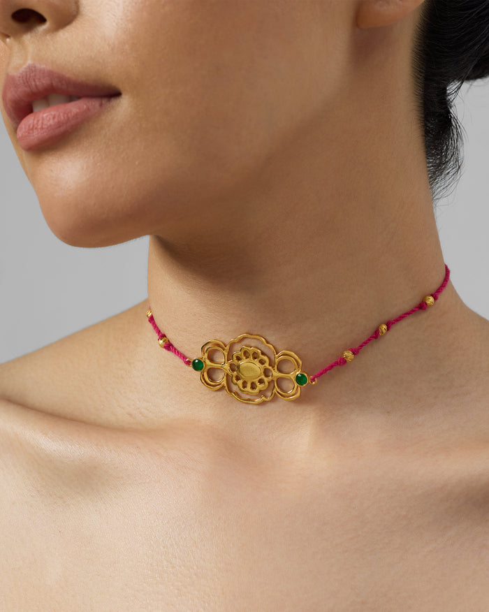 Gold titli choker with green stones worn on a magenta cord.