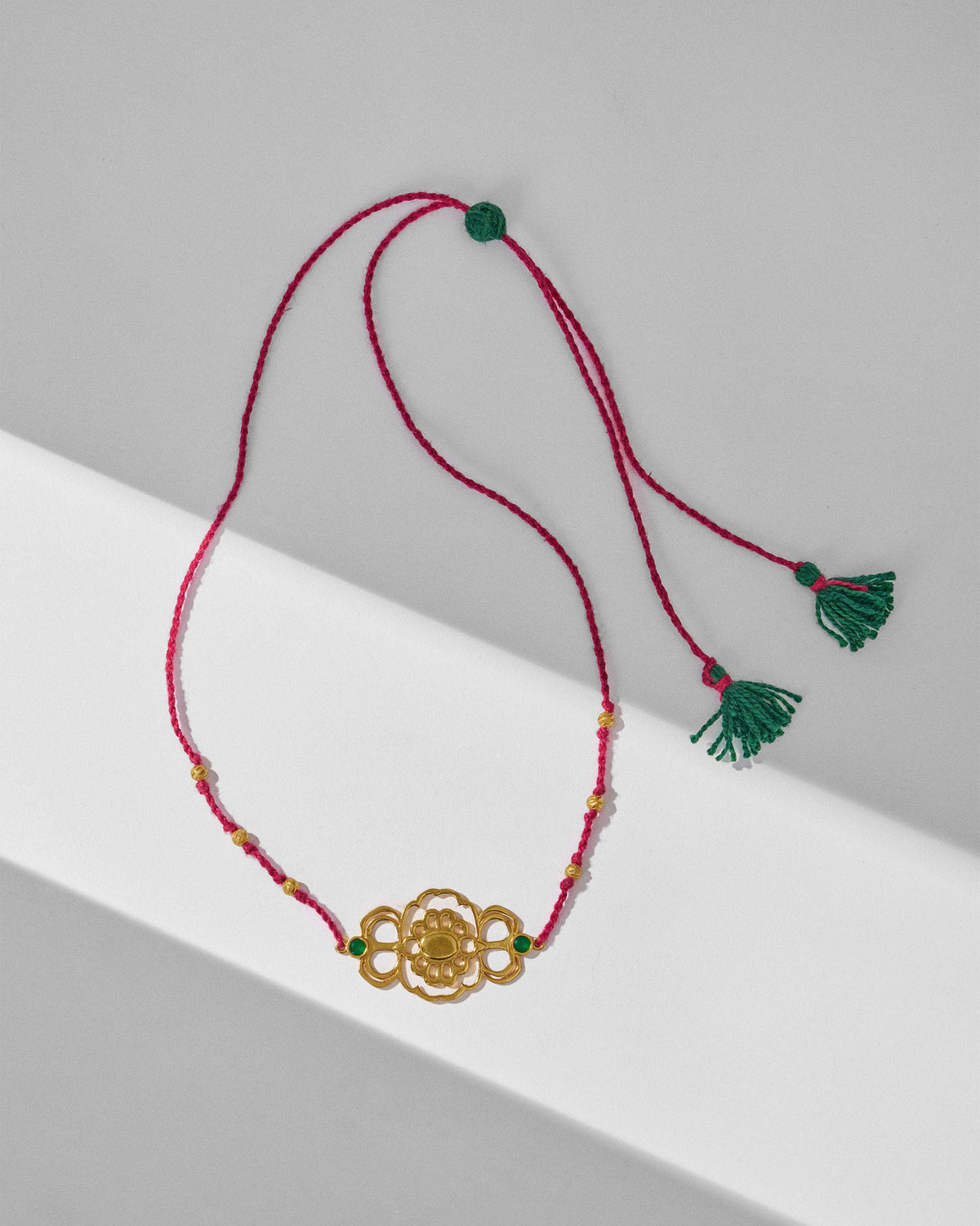 Gold titli choker laid flat on a magenta cord with green tassels.