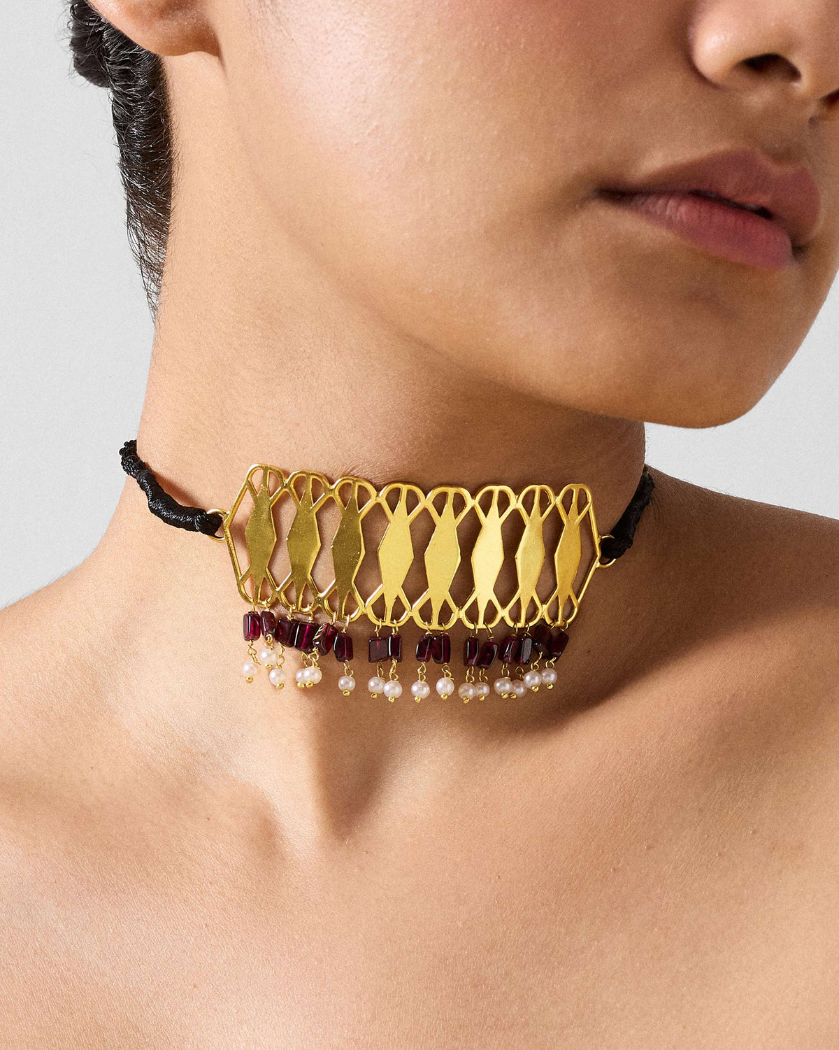Gold Barfi choker with garnet and pearl fringe worn on a black cord.