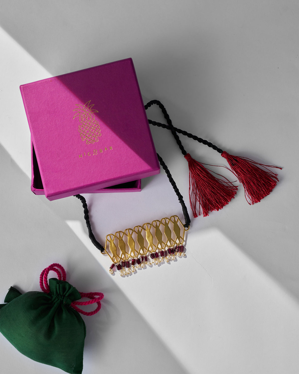 Gold Barfi choker with a magenta Nicobar gift box and green pouch.